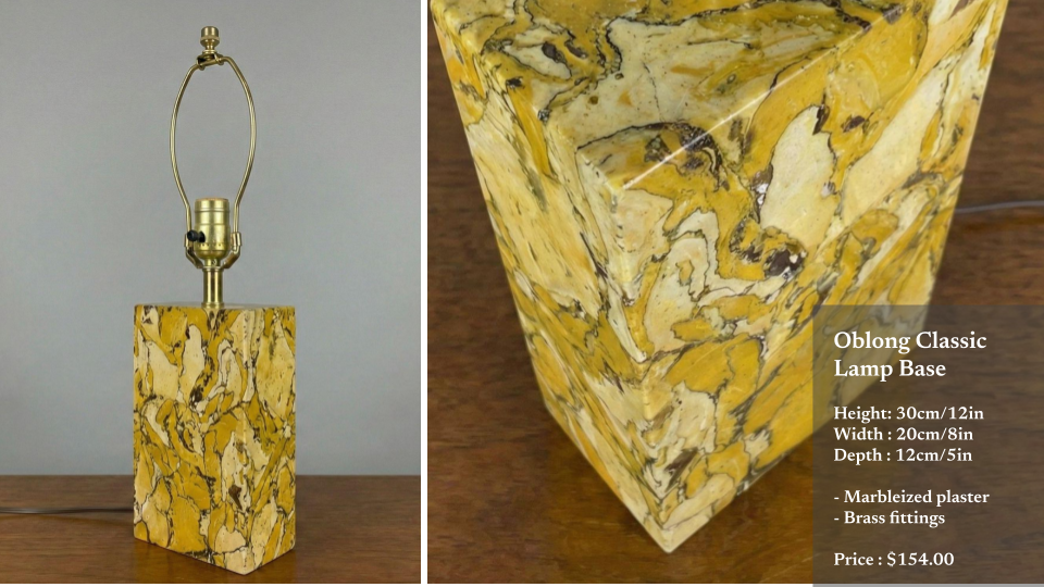 A decorative oblong classic lamp base made of marbled plaster with brass fittings, featuring a yellow, black, and cream swirling pattern. The base is placed on a wooden surface, with a lamp fixture on top, but no lampshade attached.
