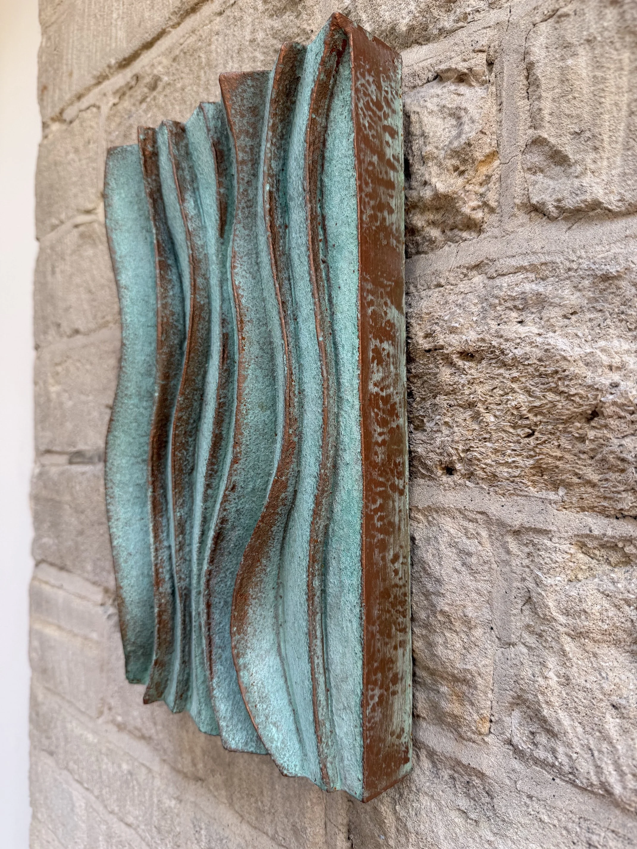 Verdigris Ripple Wave Wall Sculpture in profile against a stone wall, showing its carved wave edges