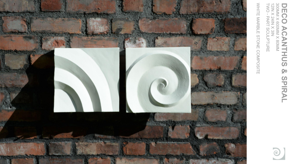 Two white marble sculpture blocks with spiral motifs, mounted on a brick wall with shadows cast to the left.