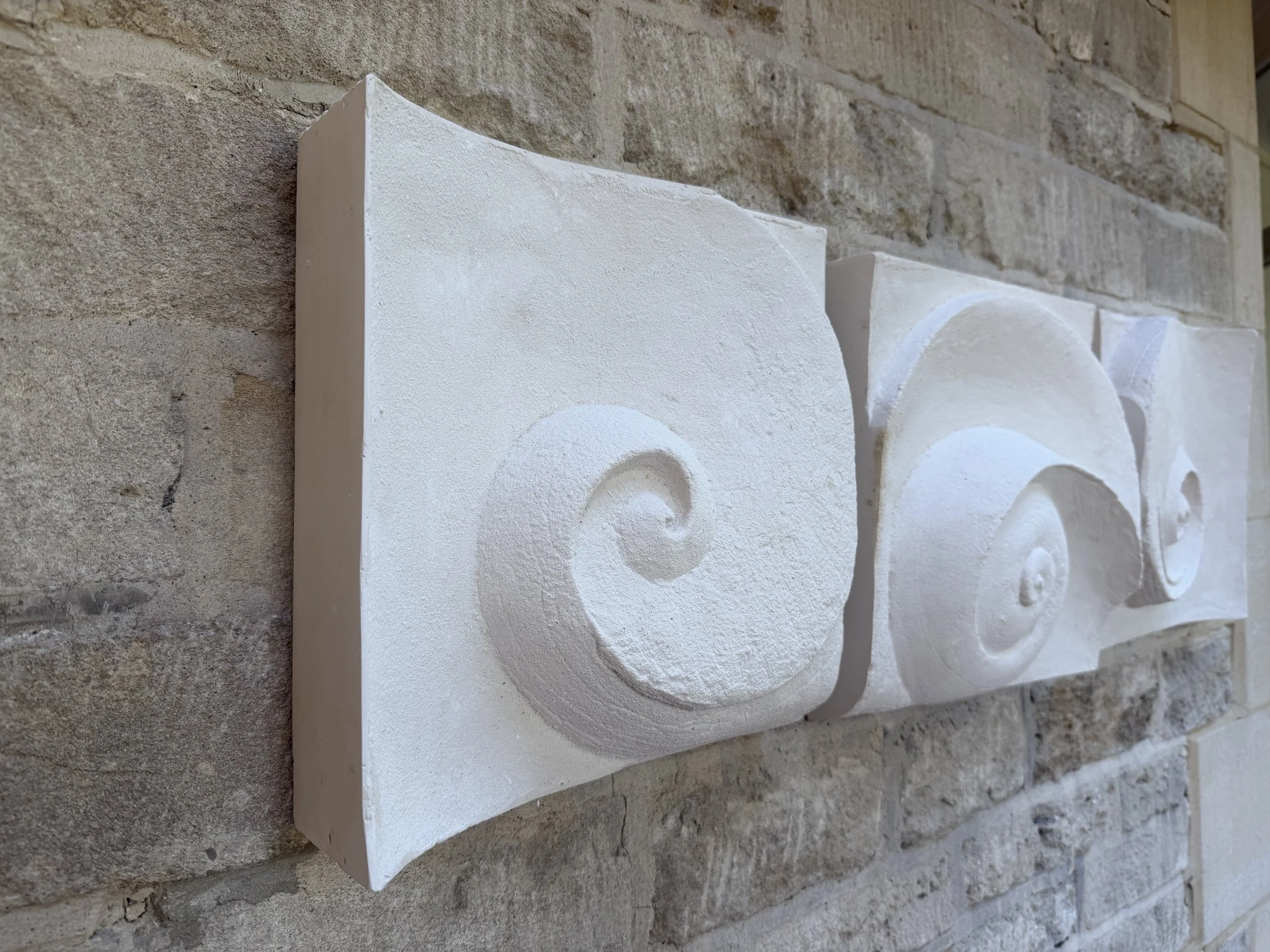 Wave Phase White Wall Sculpture panels seen in raking light along a stone wall