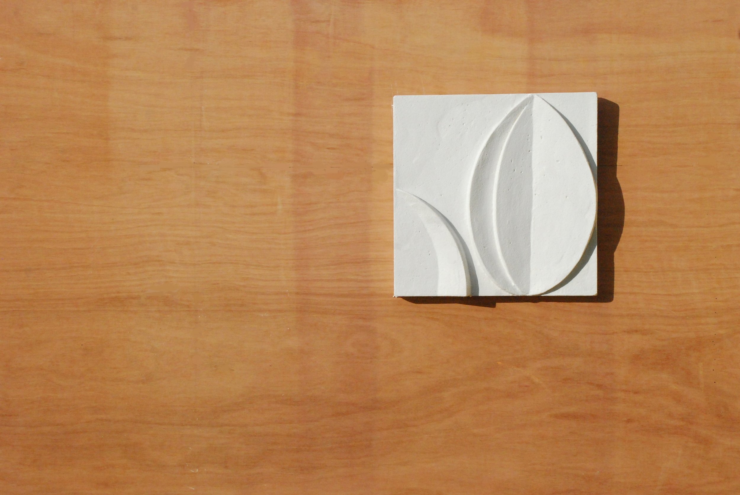 White acanthus flower wall sculpture, a square relief panel in pure white plaster, shown flat on a wooden floor