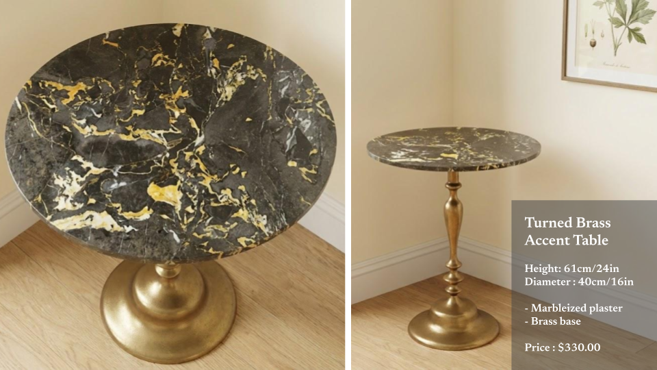 A round turned brass accent table with a black and gold marbled top, gold base, and decorative slender brass stem, situated in a corner with wooden flooring and cream-colored walls.