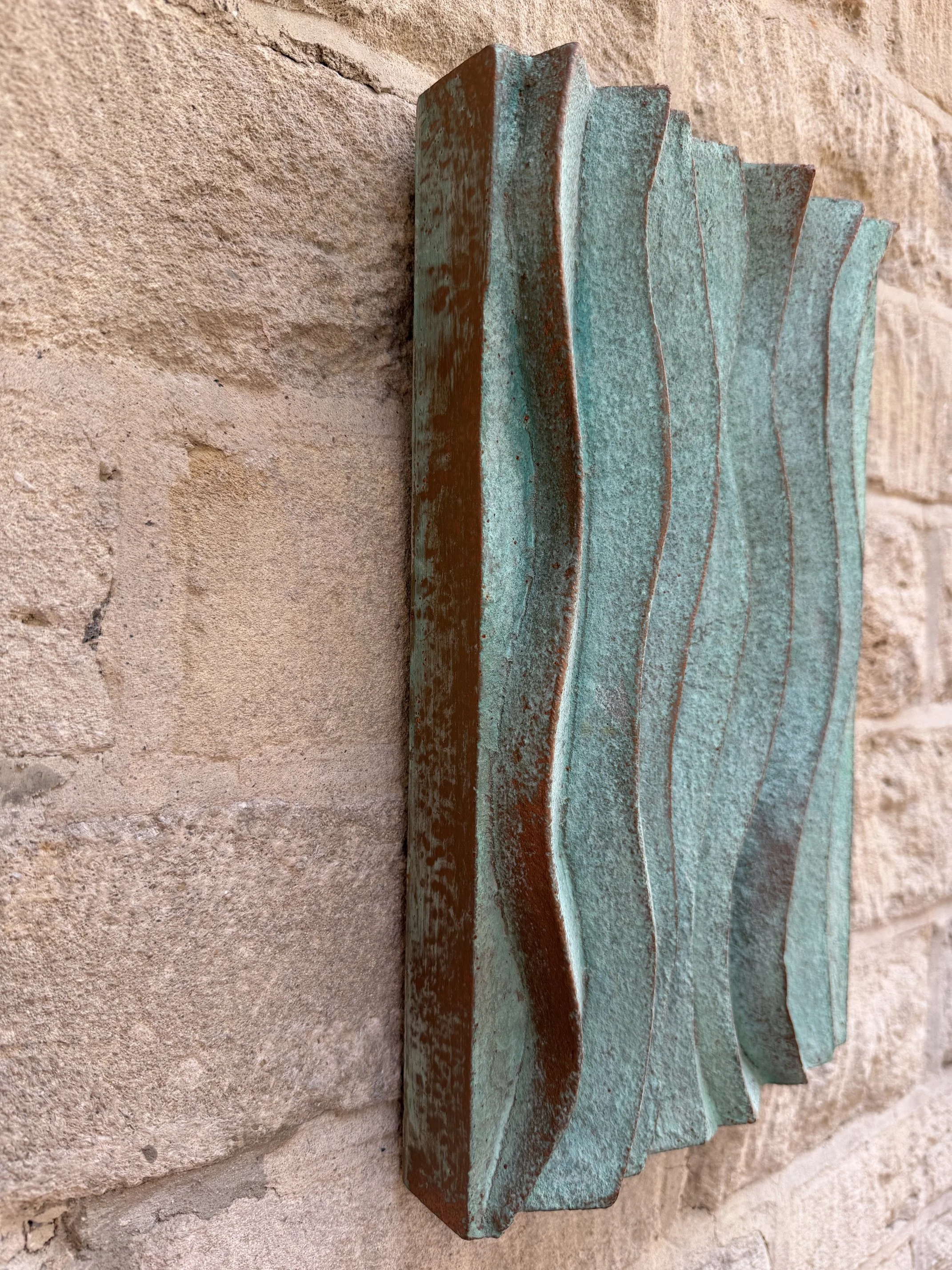 Verdigris Ripple Wave Wall Sculpture seen at an angle, showing the depth of the rippled relief