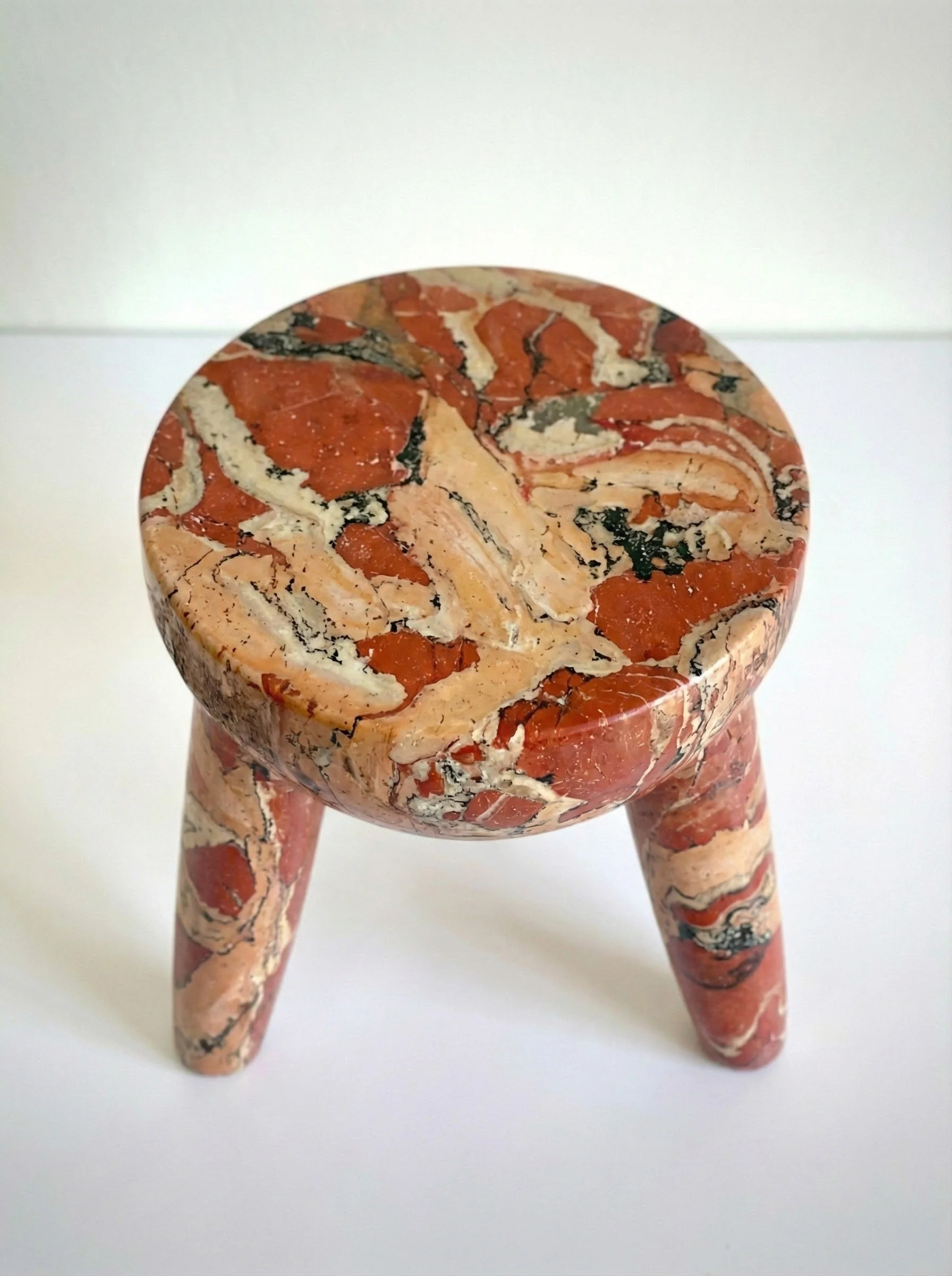 Crimson Stone Decorative Stool, a small three-legged stool in mottled crimson and cream stone finish