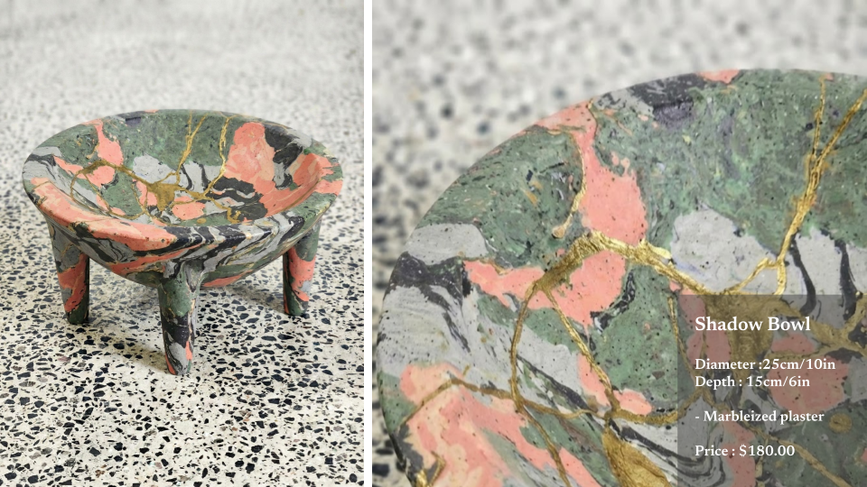 A small, marbleized plaster shadow bowl with a diameter of 25 centimeters and a depth of 15 centimeters, featuring green, peach, black, white, and gold colors, placed on a speckled black and white surface.