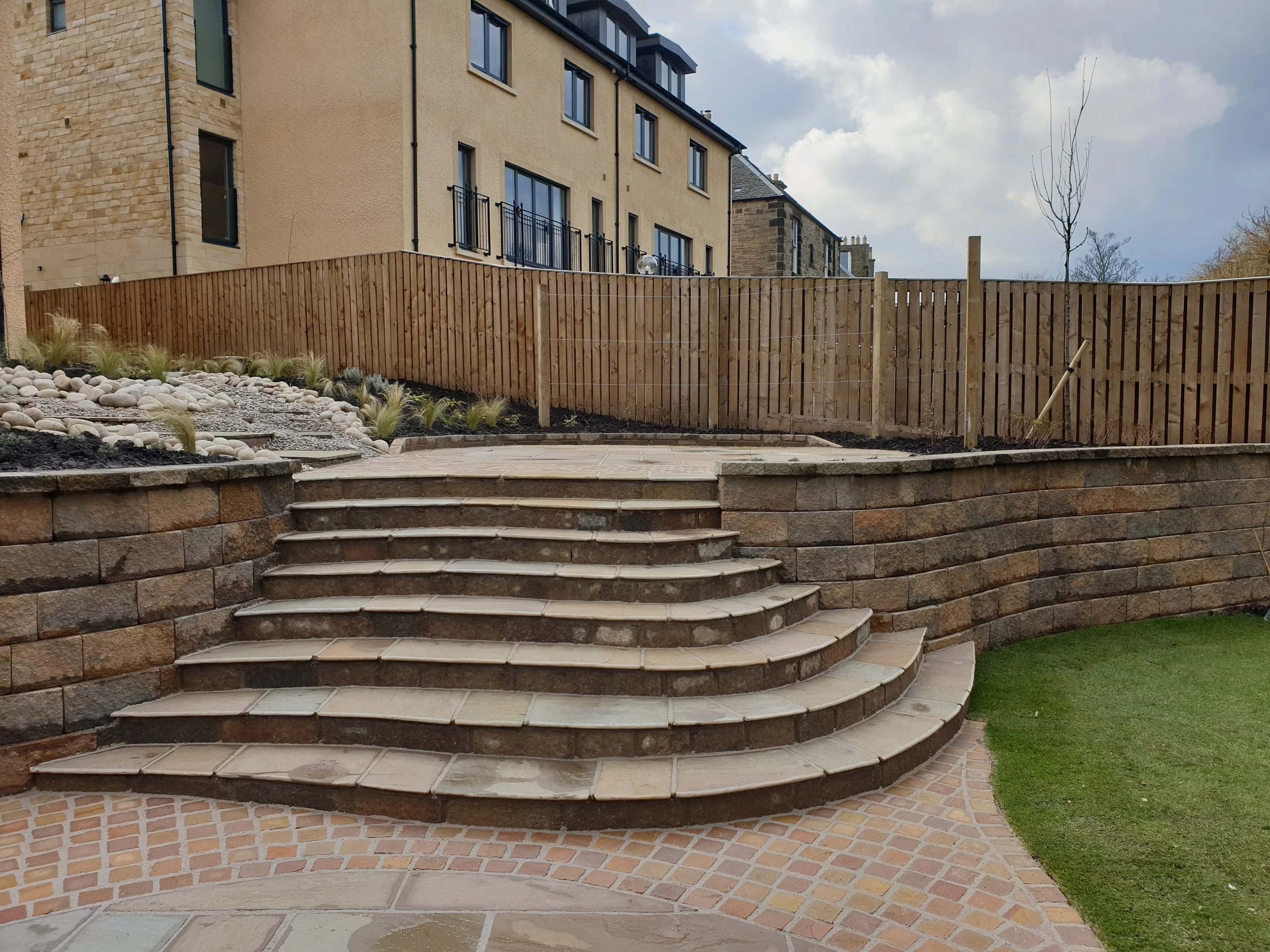 Landscaped garden with curved stone steps, raised patio and timber retaining walls.