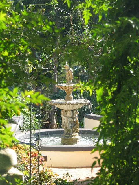 Decorative garden fountain surrounded by established planting and lush green foliage.