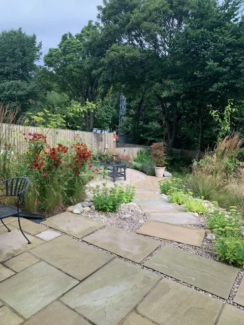 Garden landscaping with natural stone paving, planted borders, seating and mature trees.