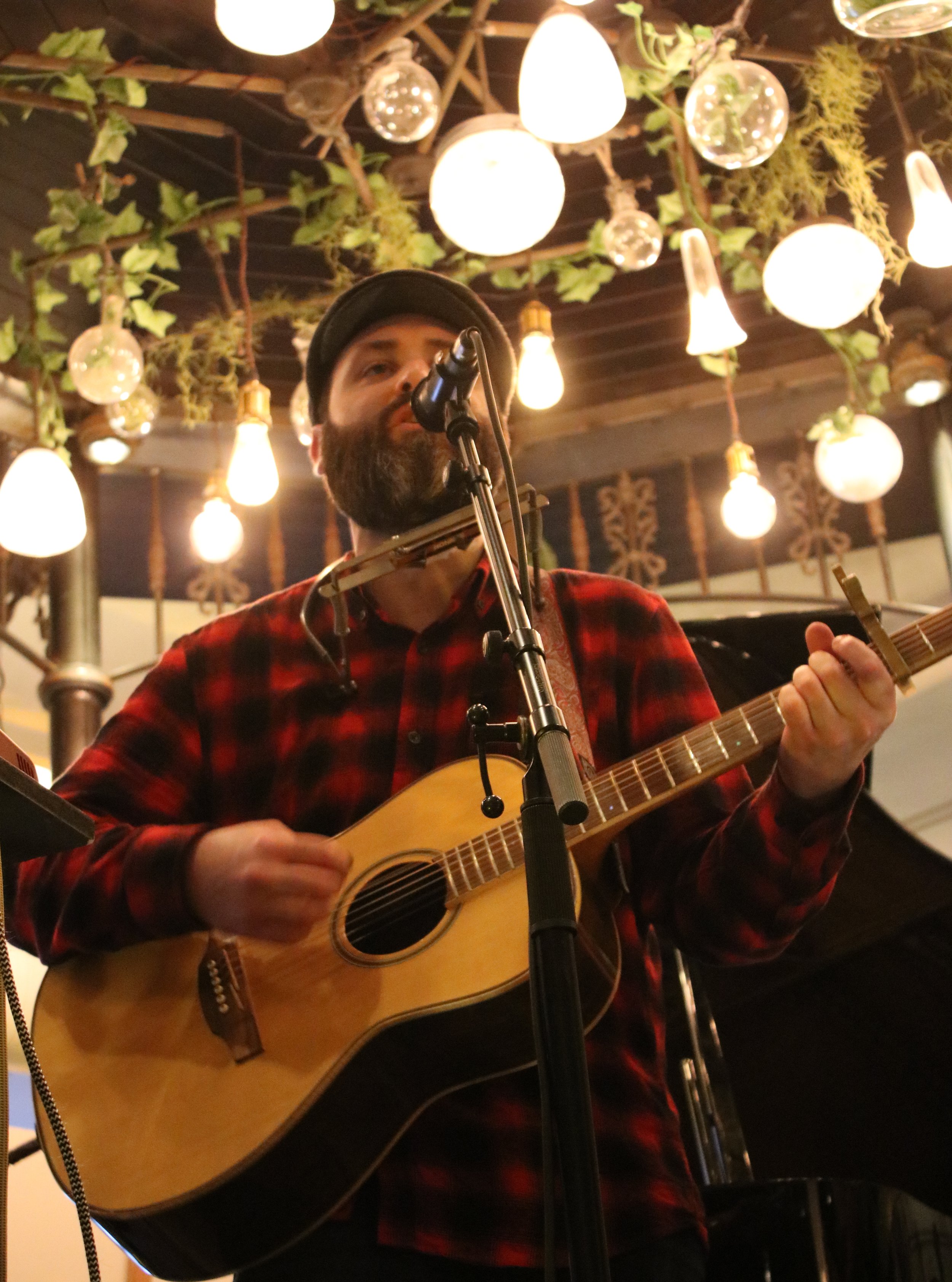 Image of Adam Sherry on stage with his guitar and harmonica around his neck