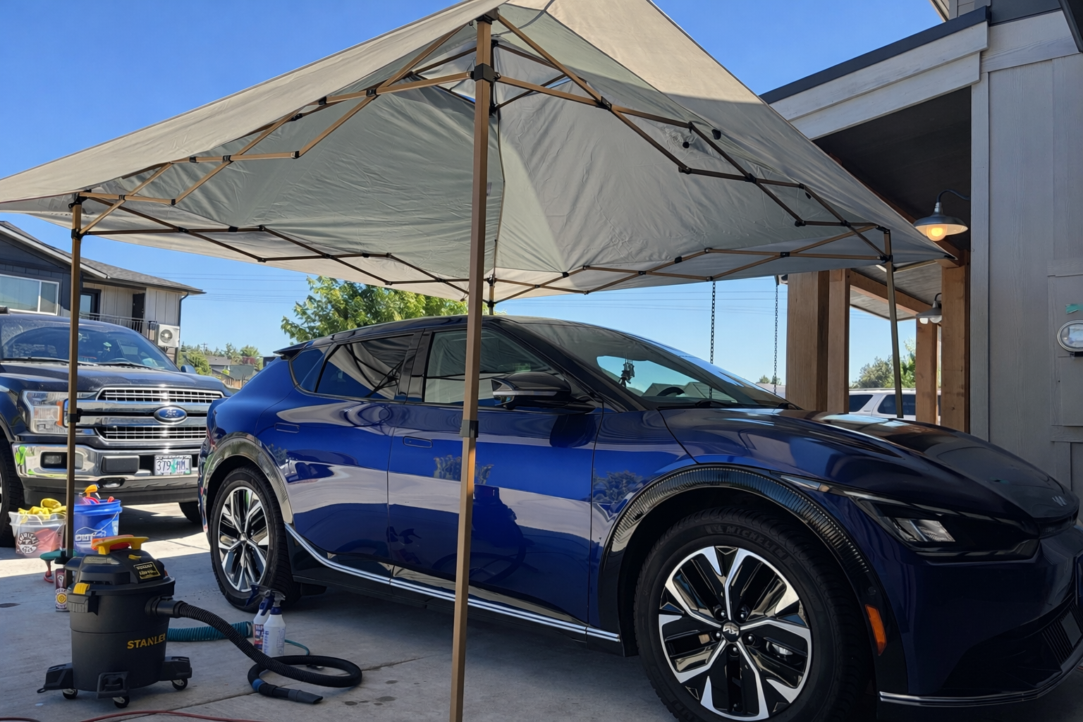 A blue Honda electric car parked outdoors under a canopy, with cleaning equipment and a black truck nearby.