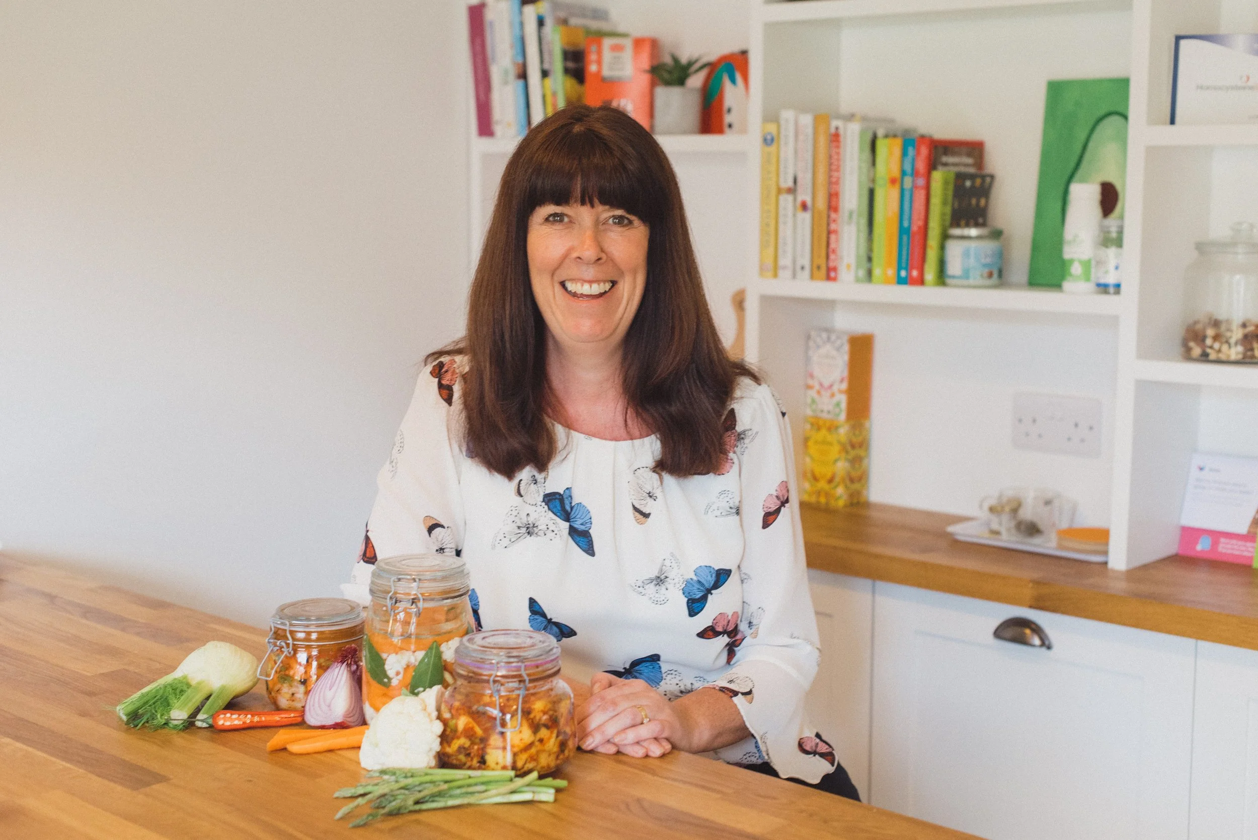 Wendy Hills, nutritional therapist in kent, digestive heath nutritionist for women over 50 sitting in her office with jars of gut health focused vegetables