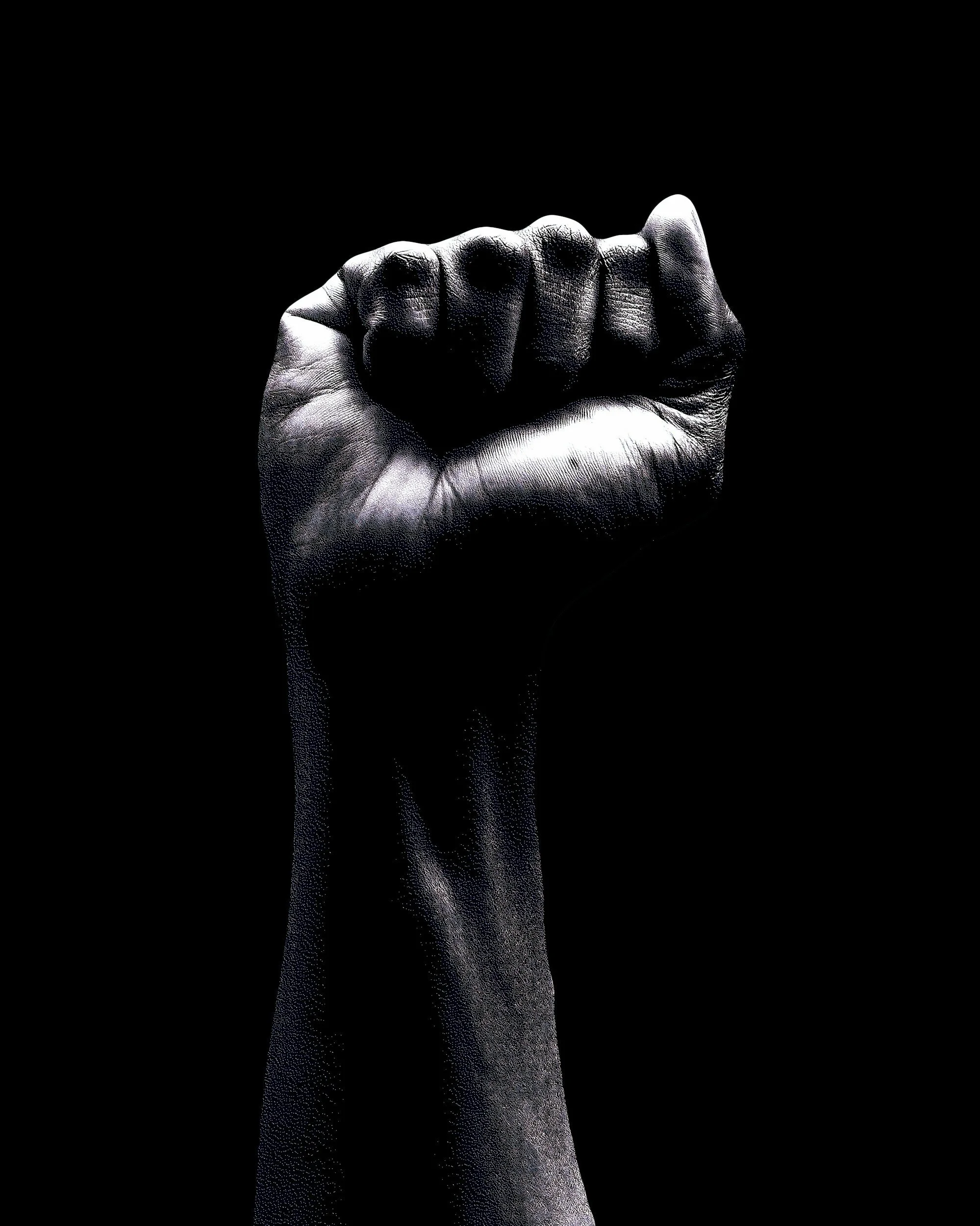 Black and white photo of a clenched fist rising into the air on a black background.