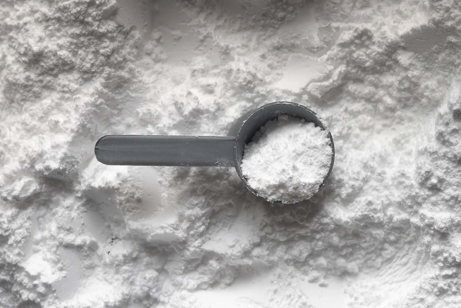 A silver scoop with creatine powder inside on top of more creatine supplement powder beneath.