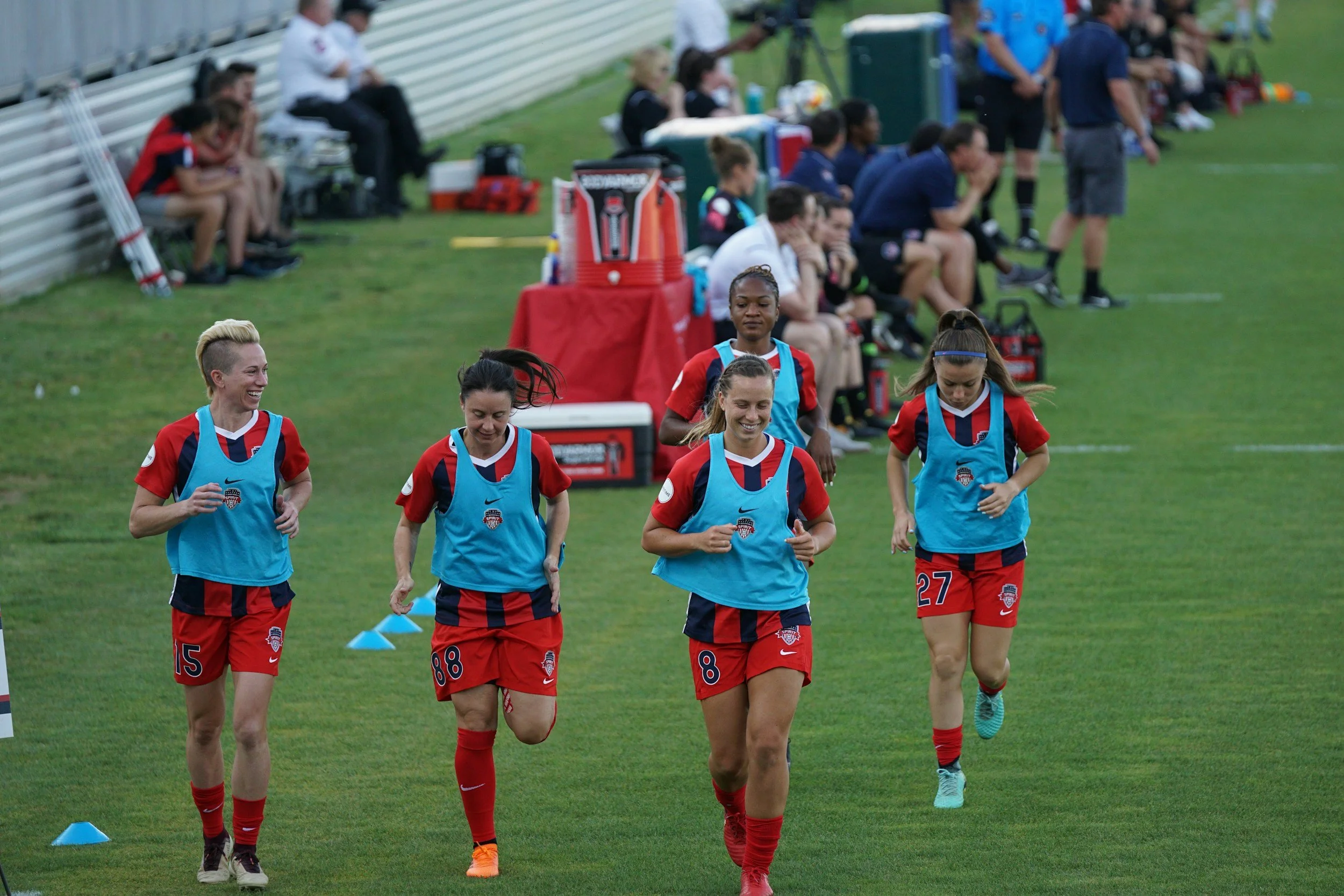 Group of female soccer players jogging together on a field in uniform while talking and warming up during training.