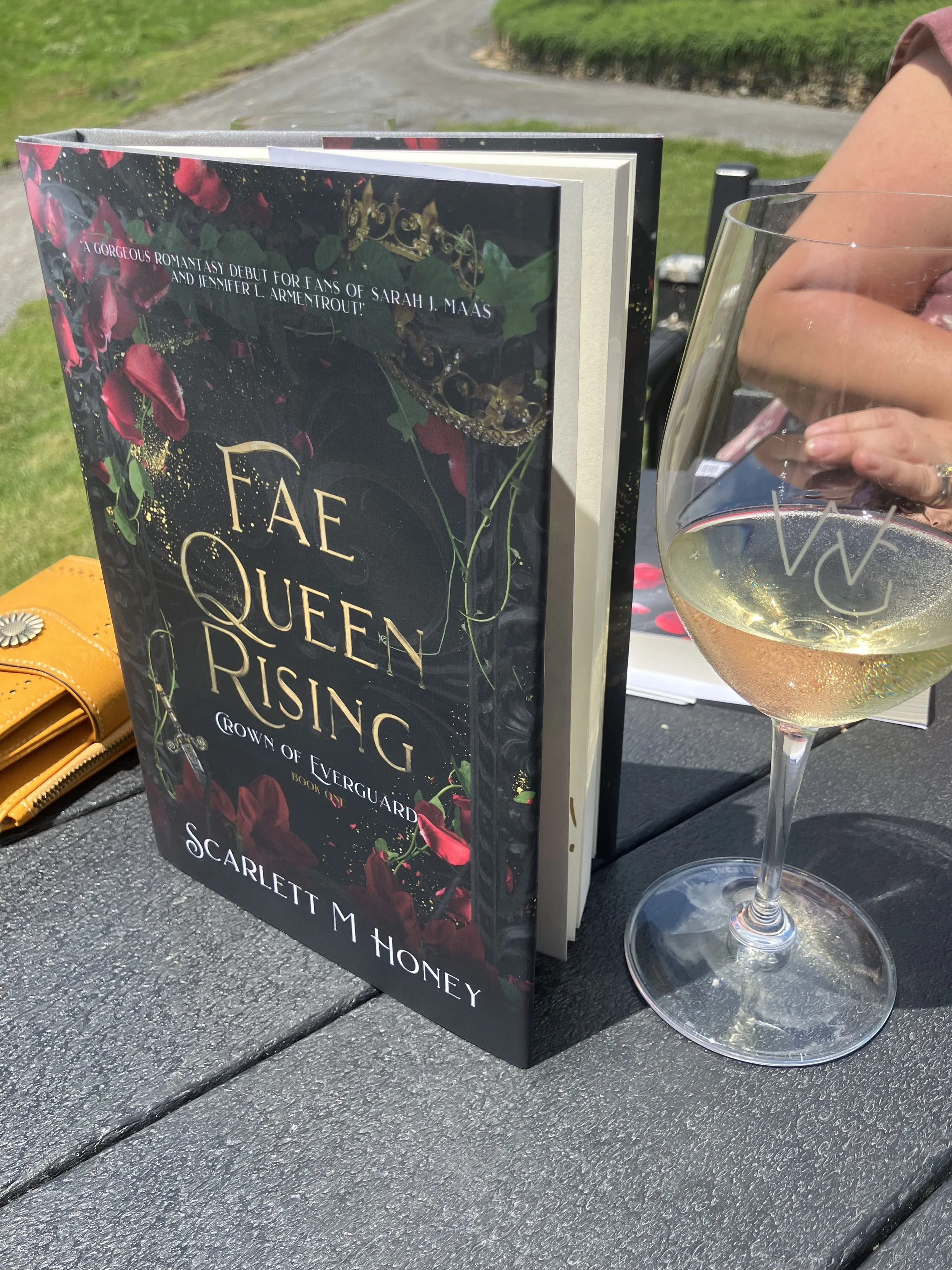 Hardcover of Fae Queen Rising next to glass of white wine