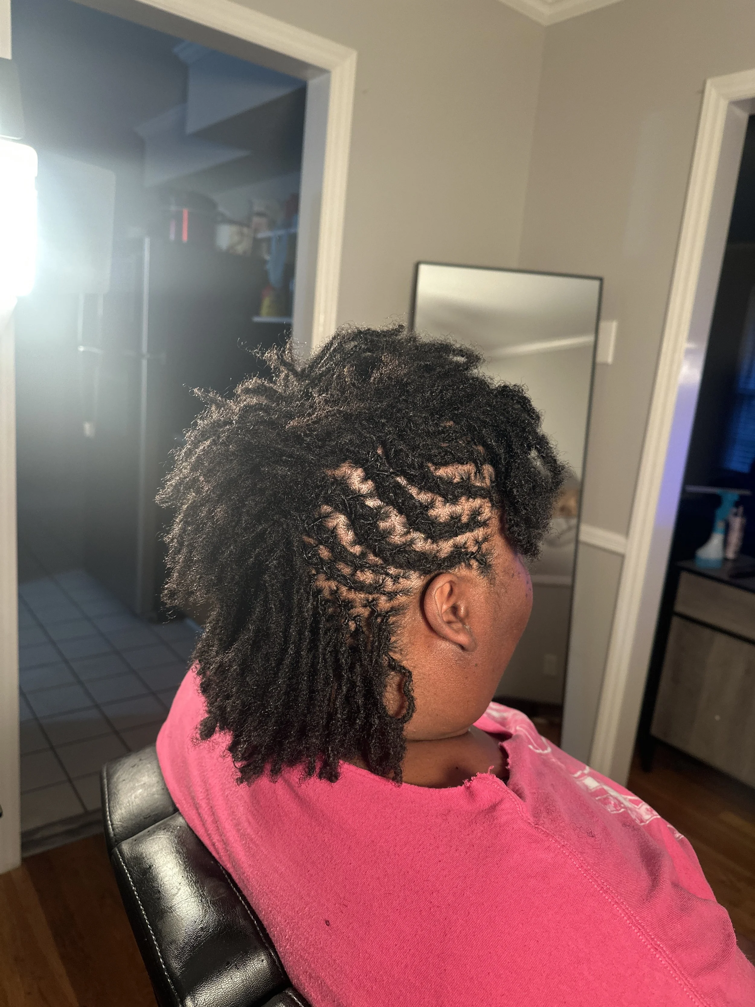 The back of a person's head with freshly styled hair in small twists, in a kitchen with wooden cabinets, a countertop with various items, and a window