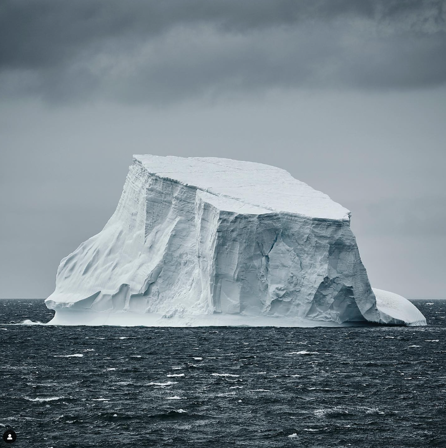 A large iceberg floating in the ocean under a cloudy sky.