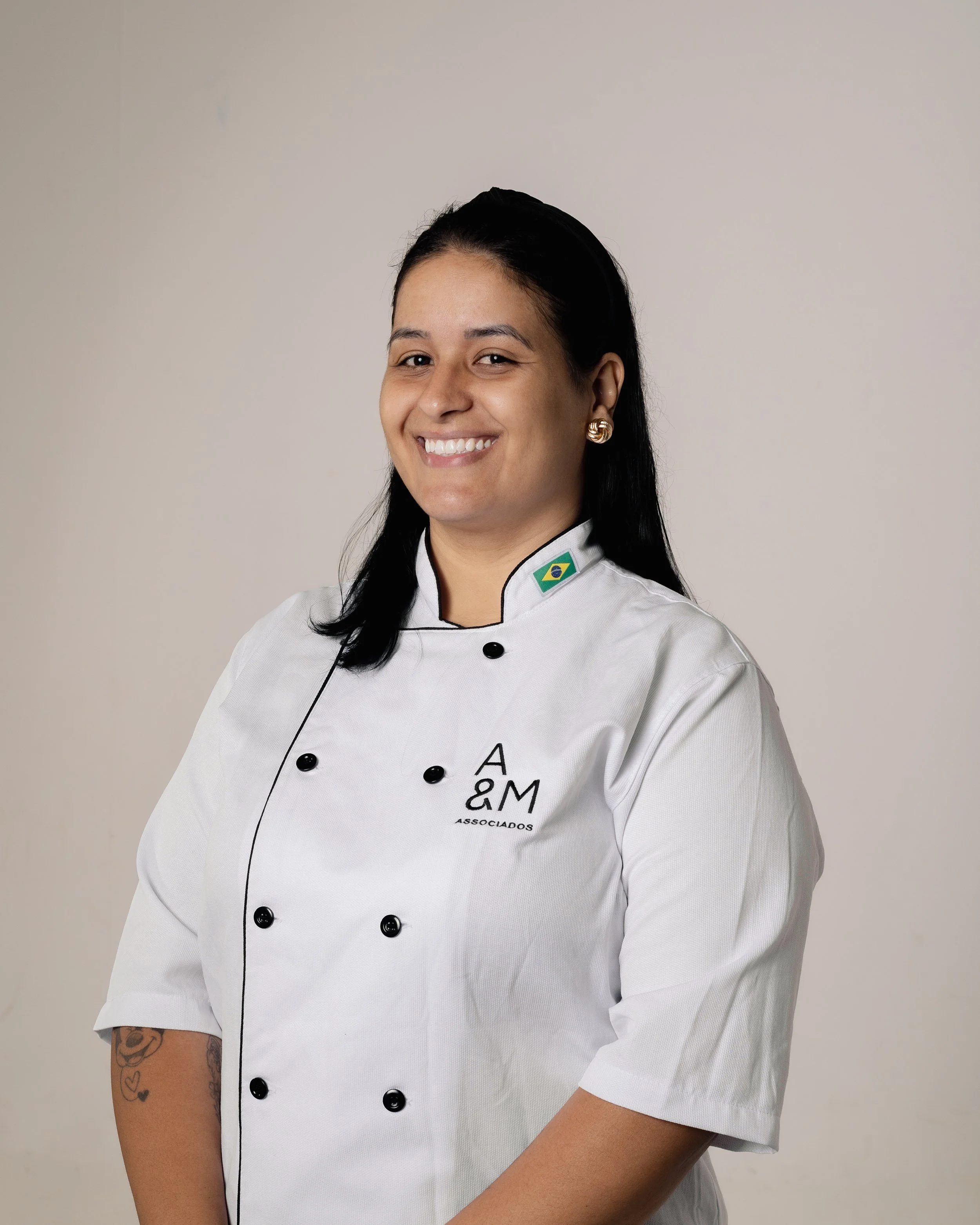 Homem sorridente de terno e gravata azul, com cabelo escuro e barba bem aparada, pose de perfil em fundo neutro.