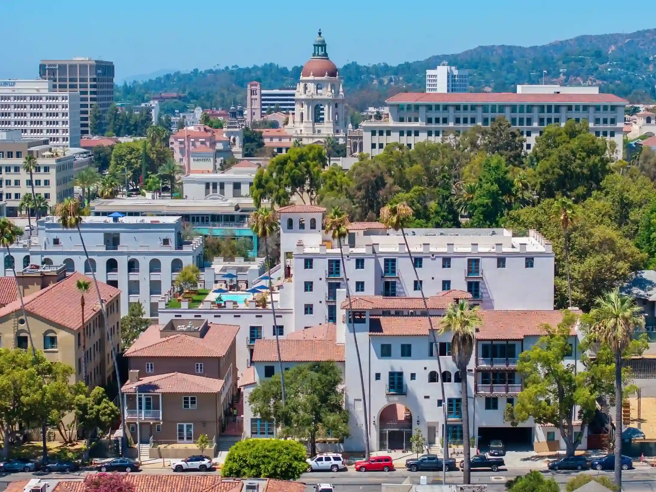 Aerial view of Catalonia in Pasadena with Spanish-style architecture, palm trees, rooftop pool, and Pasadena City Hall in the background.