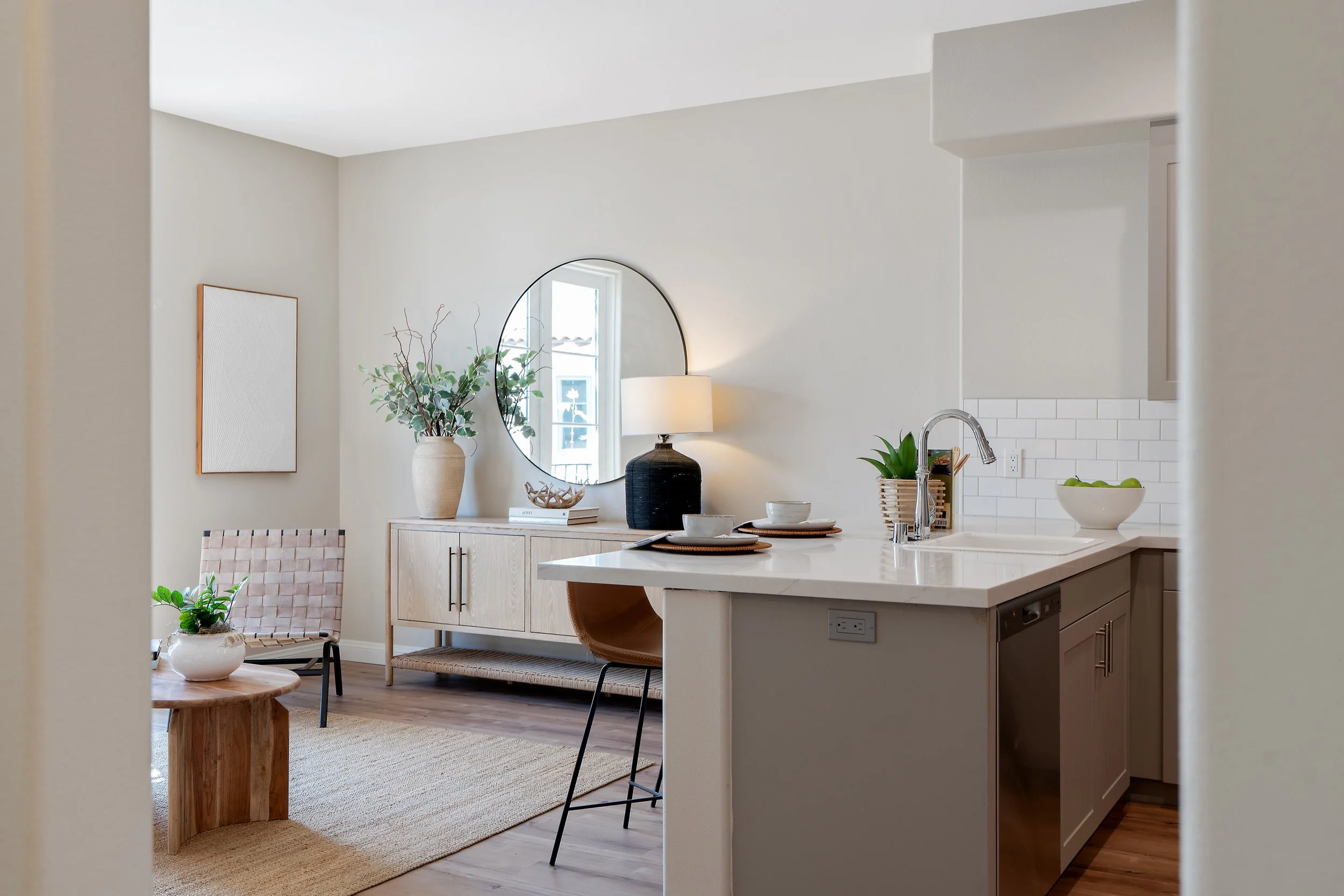 Modern kitchen and living area at Catalonia Apartments in Pasadena, CA, featuring a white island, subway tile backsplash, wood-style flooring, and neutral decor.