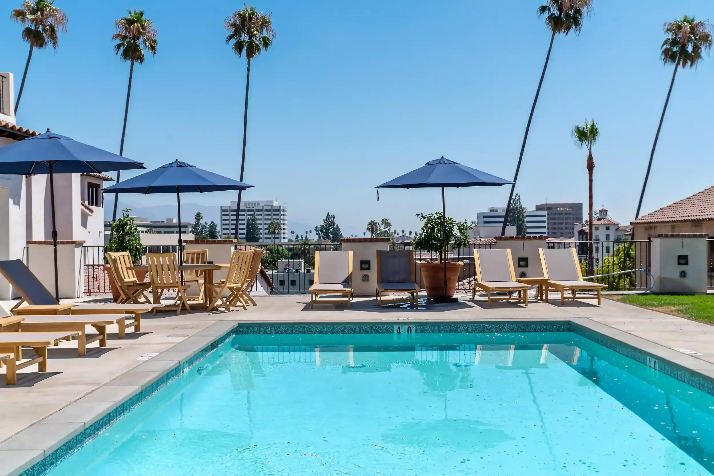 Poolside lounge area at Catalonia in Playhouse Village, Pasadena, CA, featuring lounge chairs, umbrellas, palm trees, and city views.