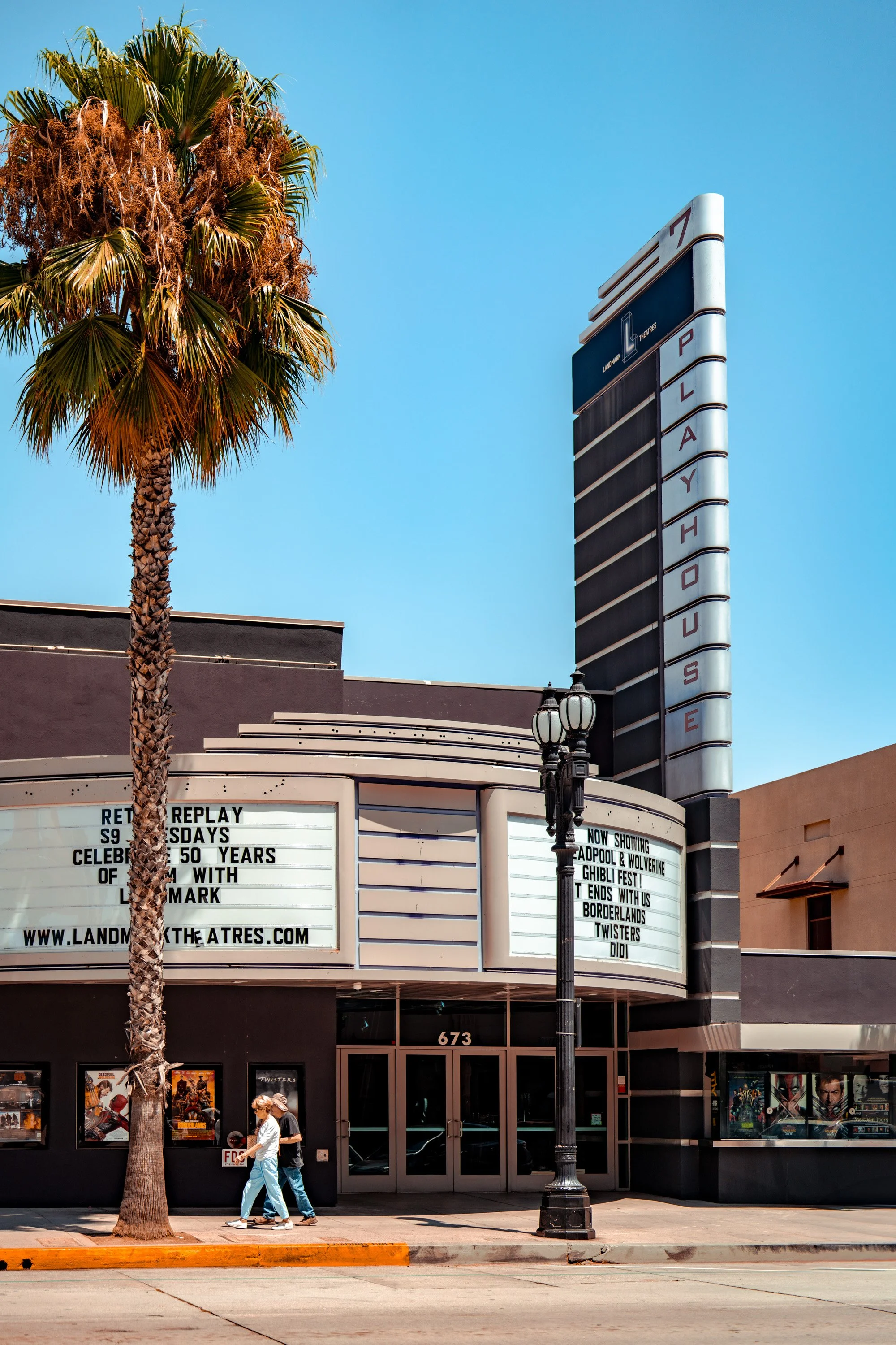 Landmark Pasadena Playhouse movie theater exterior with marquee, palm tree, and pedestrians on a sunny Pasadena street.
