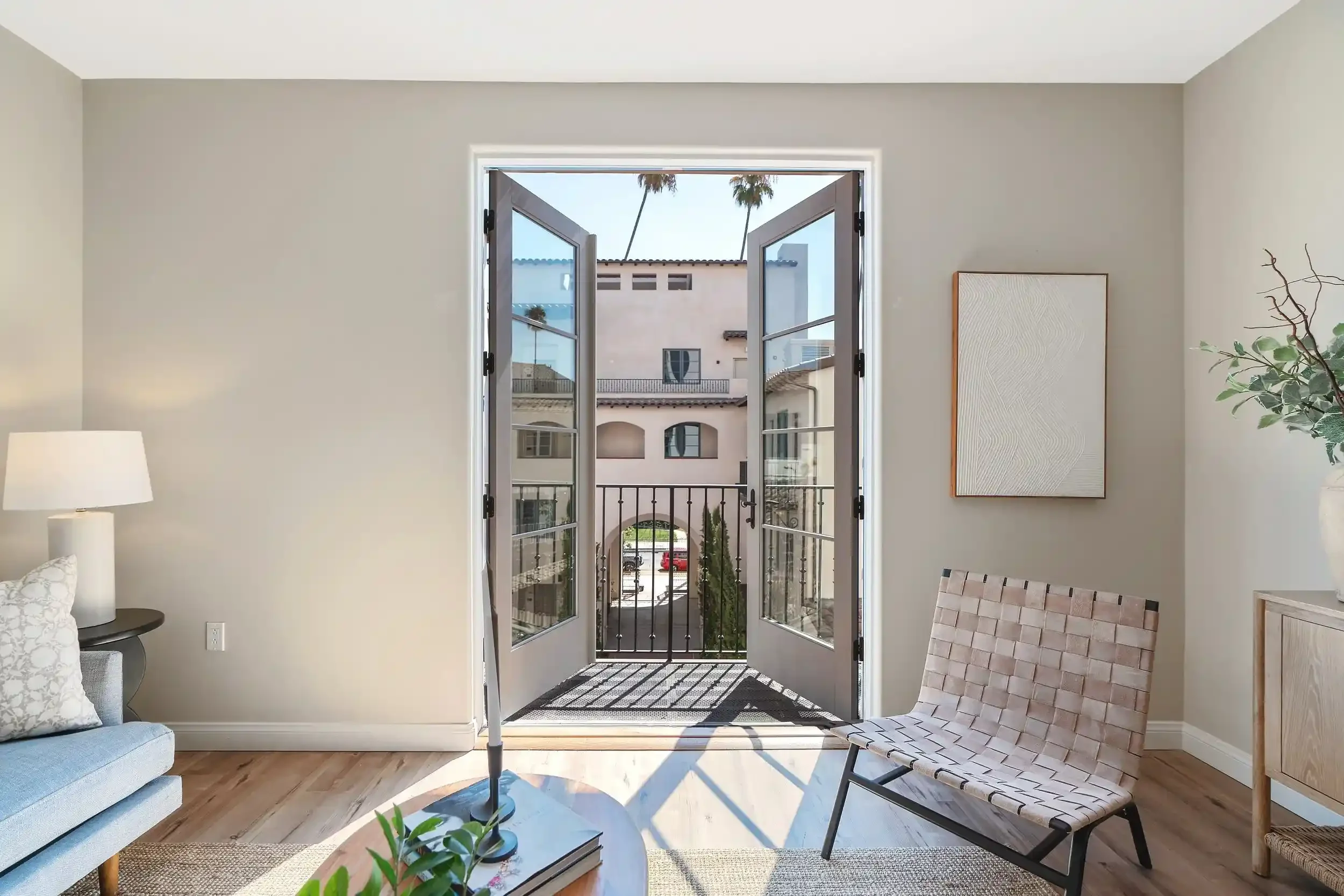 Bright apartment living room at Catalonia featuring French doors, a Juliet balcony, wood-style flooring, neutral decor, and natural light.