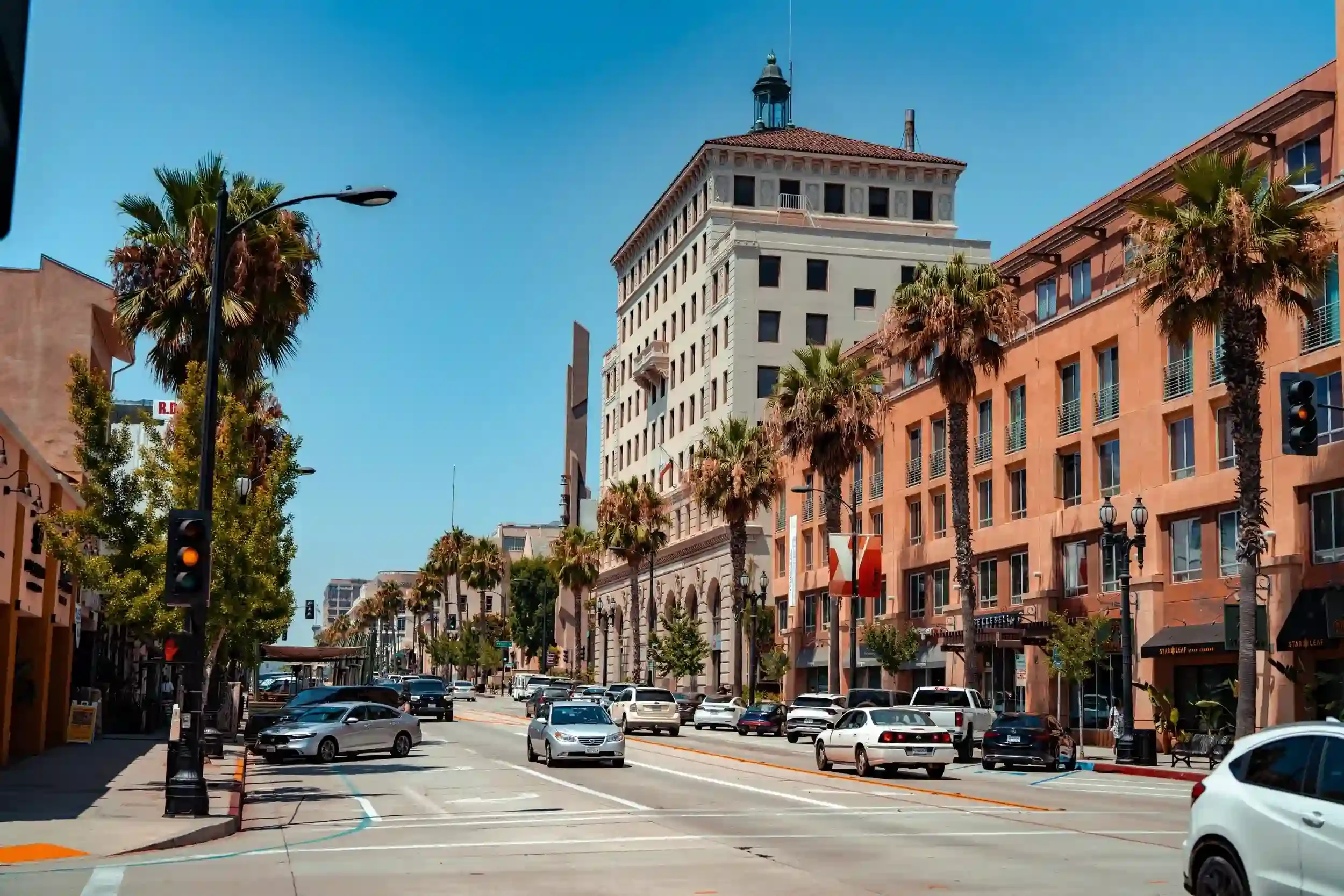 Street view of downtown Pasadena with palm trees, historic buildings, storefronts, and traffic along a sunny city street.
