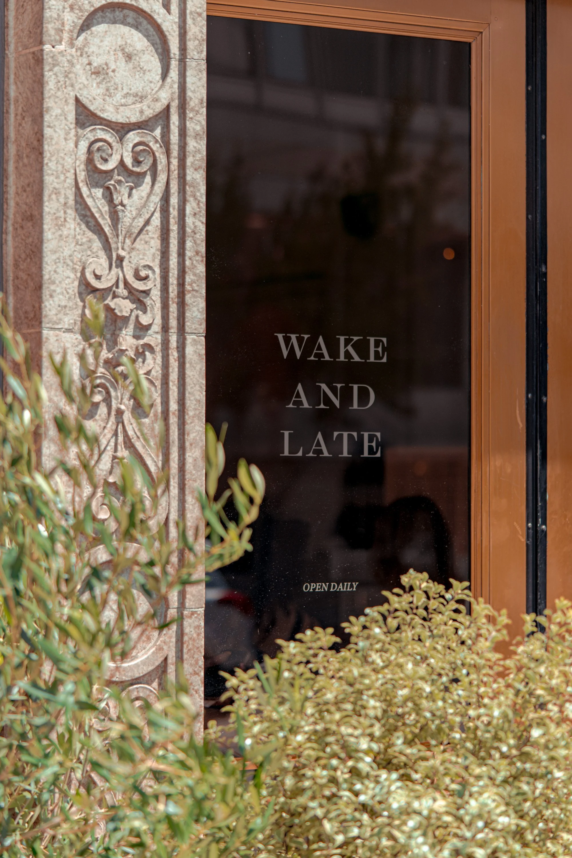 Wake and Late storefront window in Pasadena with decorative stone detail and greenery.