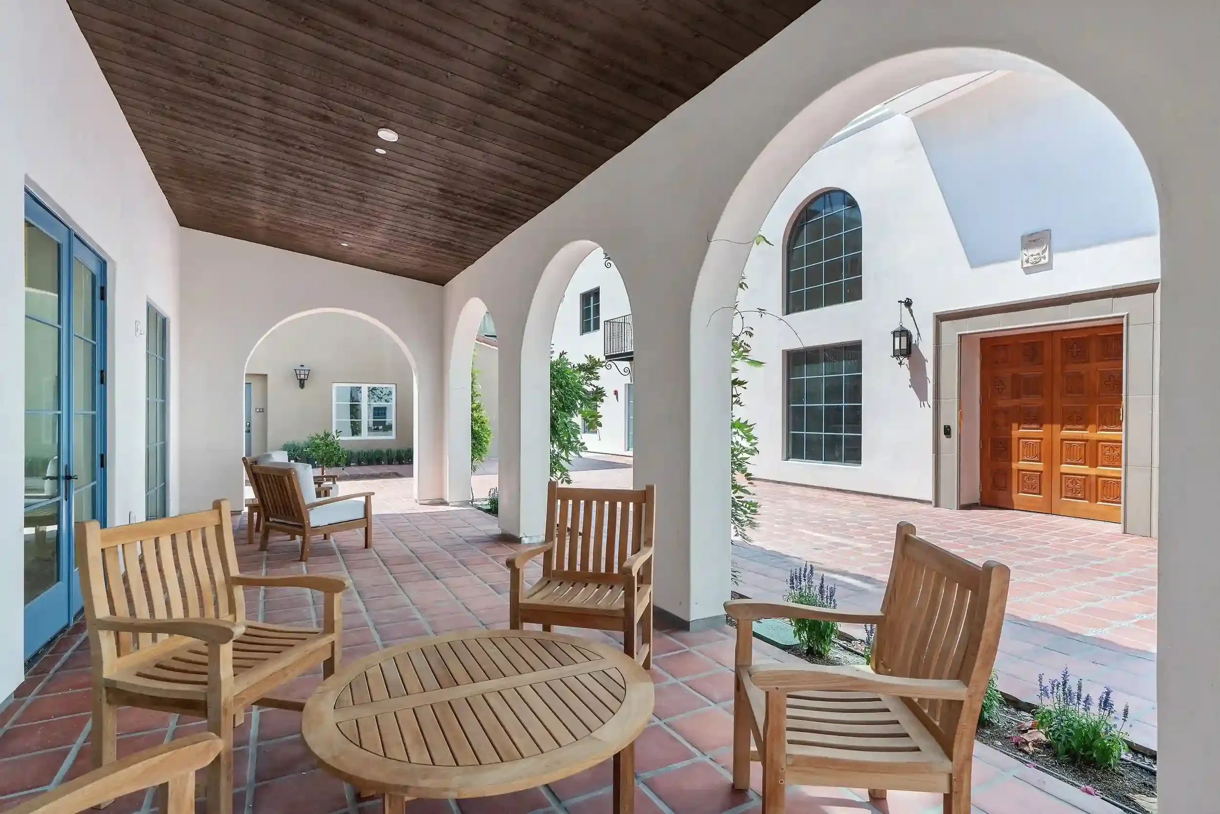 Catalonia courtyard seating area with arched walkways, wood chairs, terra cotta tile, blue doors, and Spanish-style architecture.