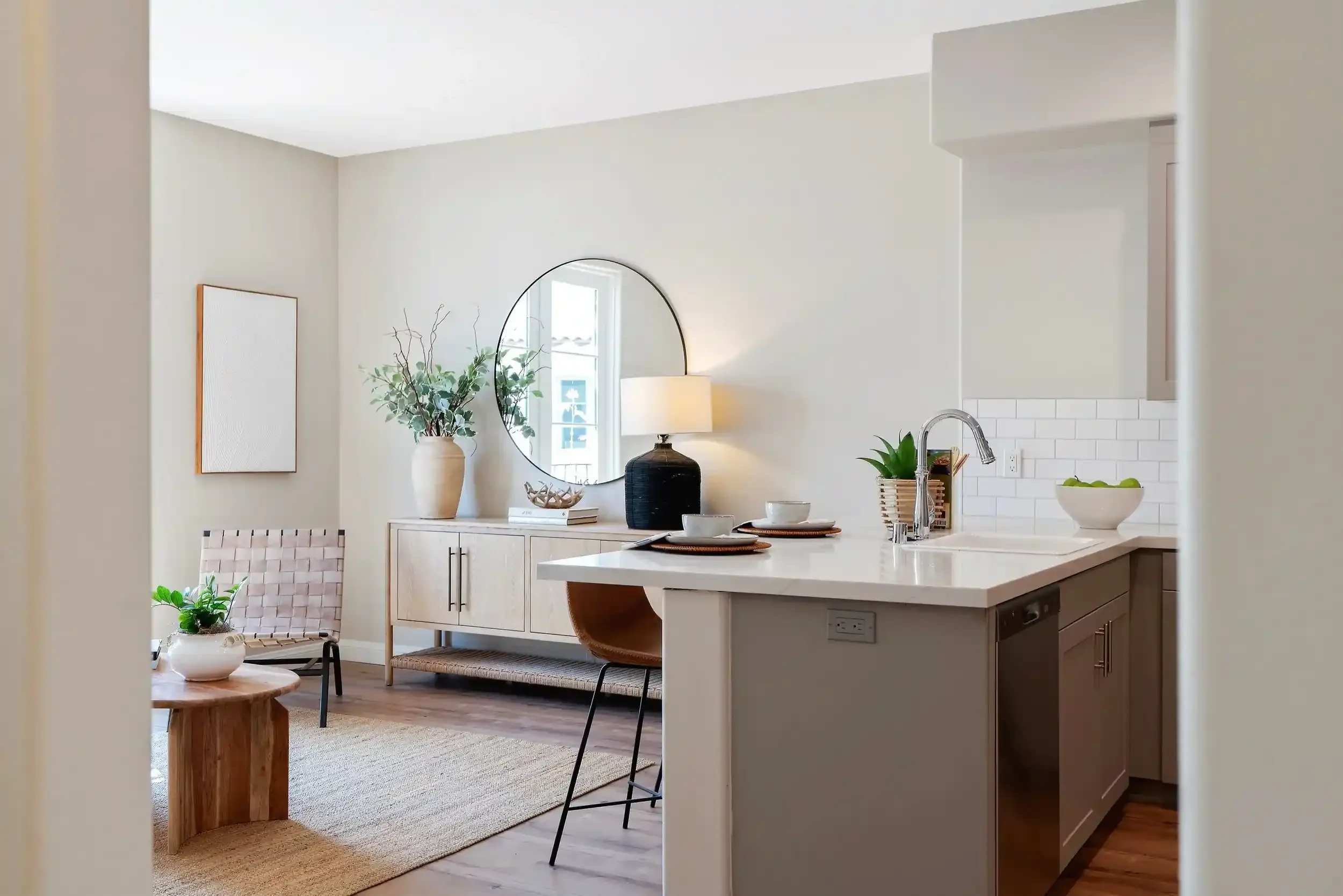 Modern apartment kitchen and living area at Catalonia featuring a white island, subway tile backsplash, wood-style flooring, neutral decor, and natural light.