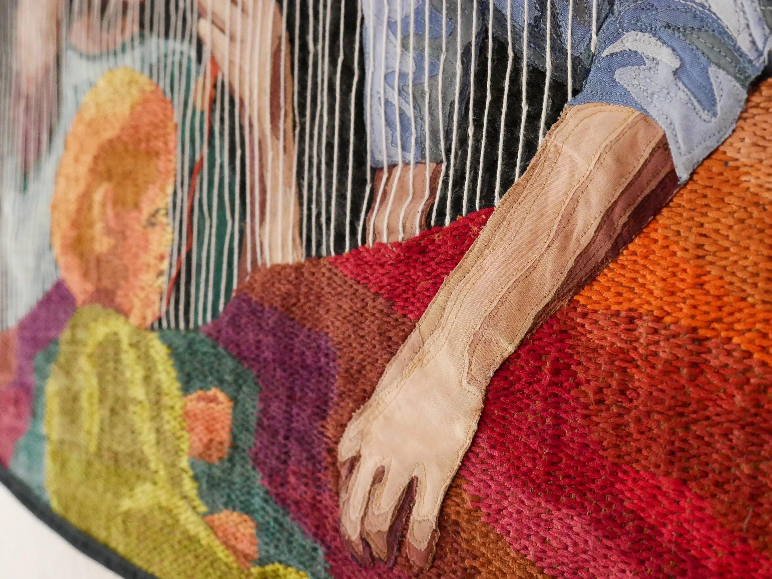 Quilt detail of a woman's hand reaching through the warp strings of a weaving toward the infant the weaving depicts