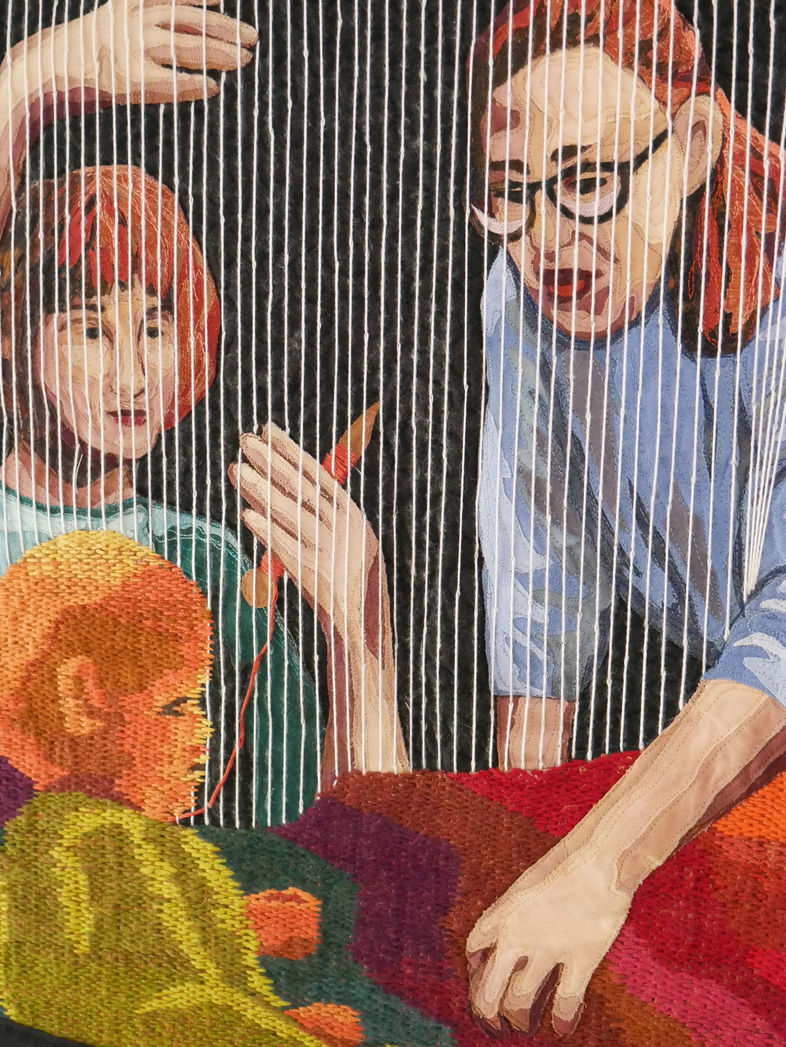 two women sitting behind the warp strings of a weaving of an infant baby surrounded in blended warm tones.