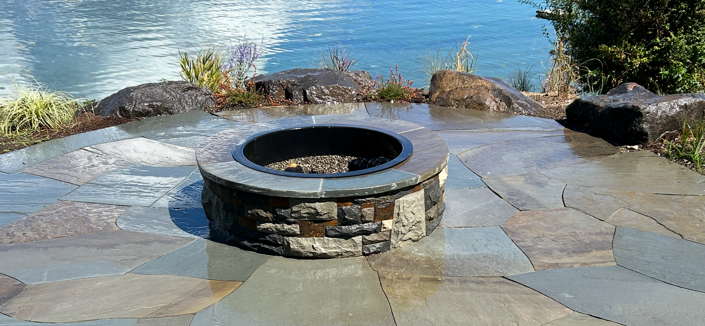 A bluestone patio with a circular handmade custom fire table in Gig Harbor crafted by 7 Lamps Construction. 7lamps.com
