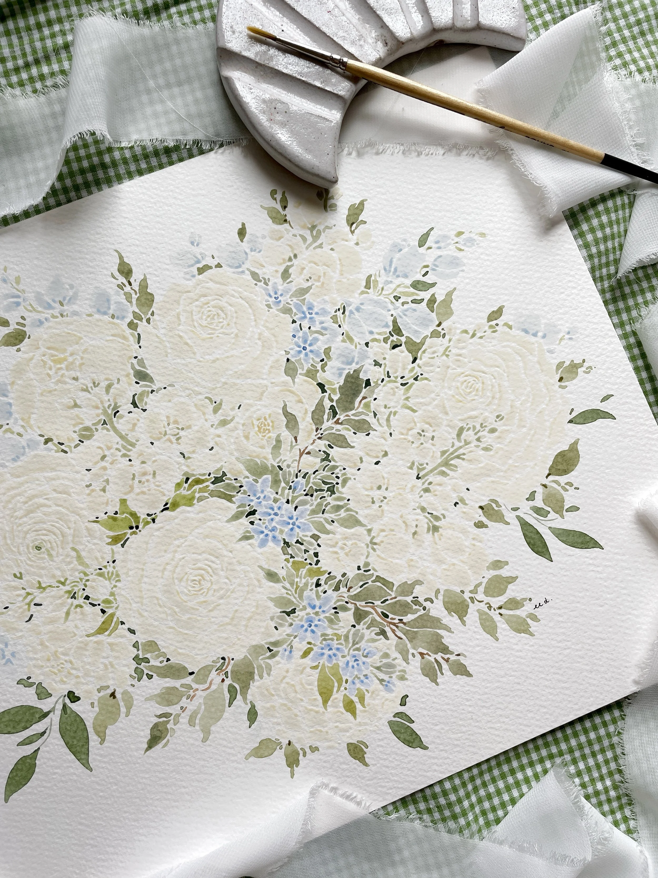 Watercolor floral painting of white roses and blue flowers with green leaves on textured paper, surrounded by a green gingham cloth, white fabric, a partial gray ceramic palette, and a paintbrush.