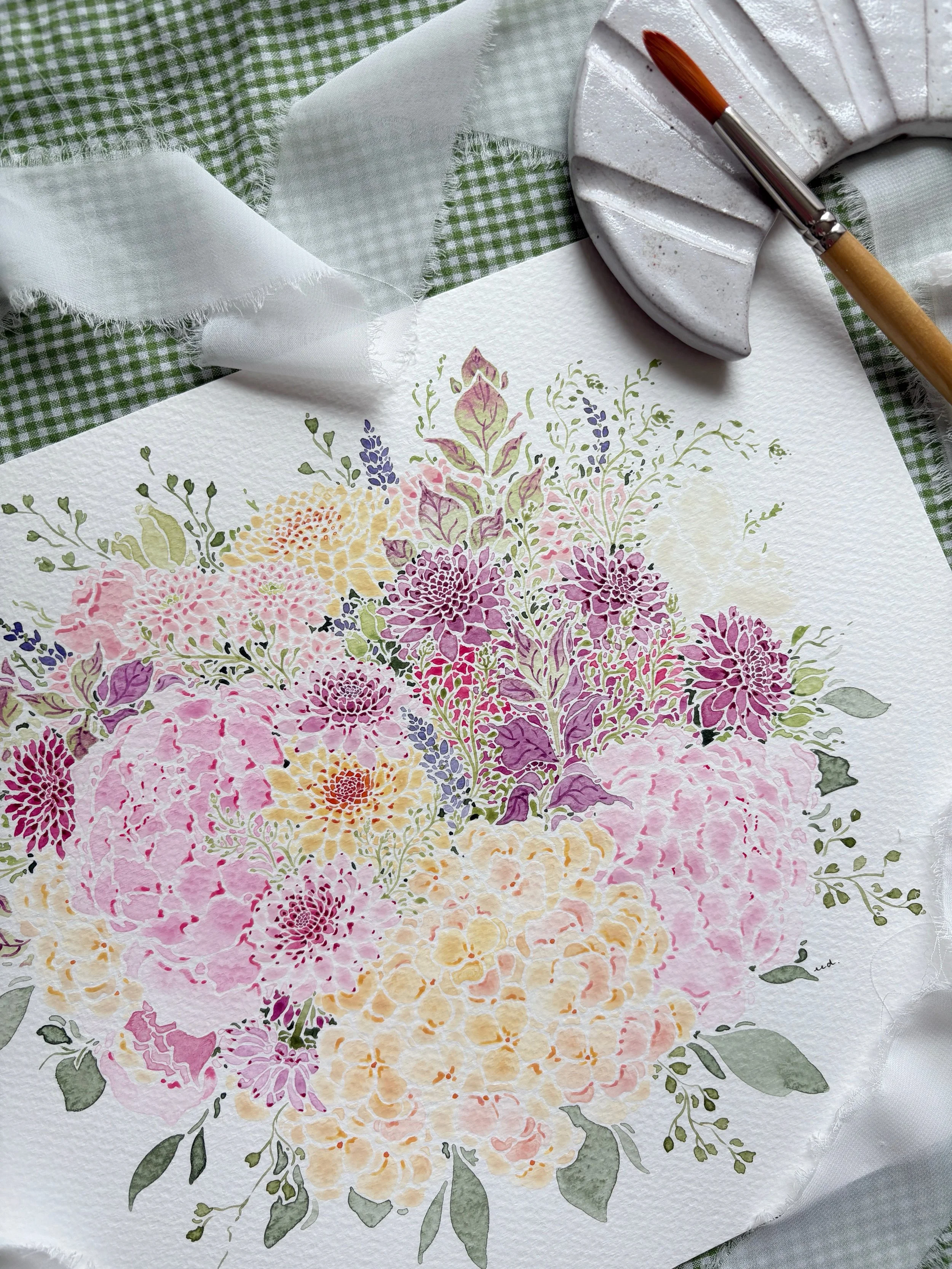Watercolor floral painting of pink, purple, yellow, and cream flowers on textured paper, with a paintbrush and ceramic palette on a green checkered cloth with white ribbon.