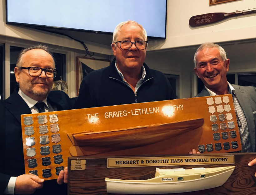 Gus Kinnear (centre), owner of Krishna, with the trophies won by his boat and crew during the 2025-2026 Metung Yacht Club senior fleet competing season. Kinnear is with Andrew Lethlean (left) and Fred Haes (right), helping him to hold the weight of T