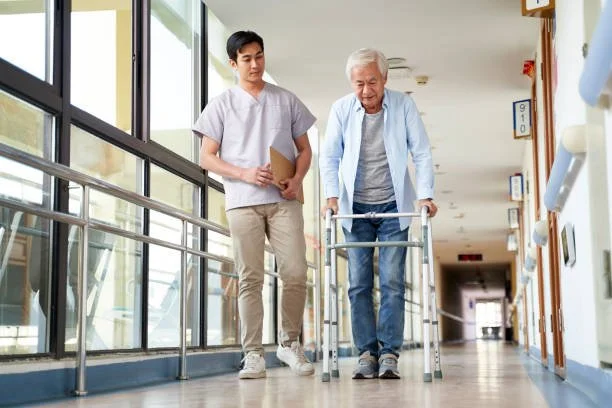 Young caregiver supporting an elderly man using a walker during a physiotherapy session in a healthcare facility corridor with Potentiate Rehab.