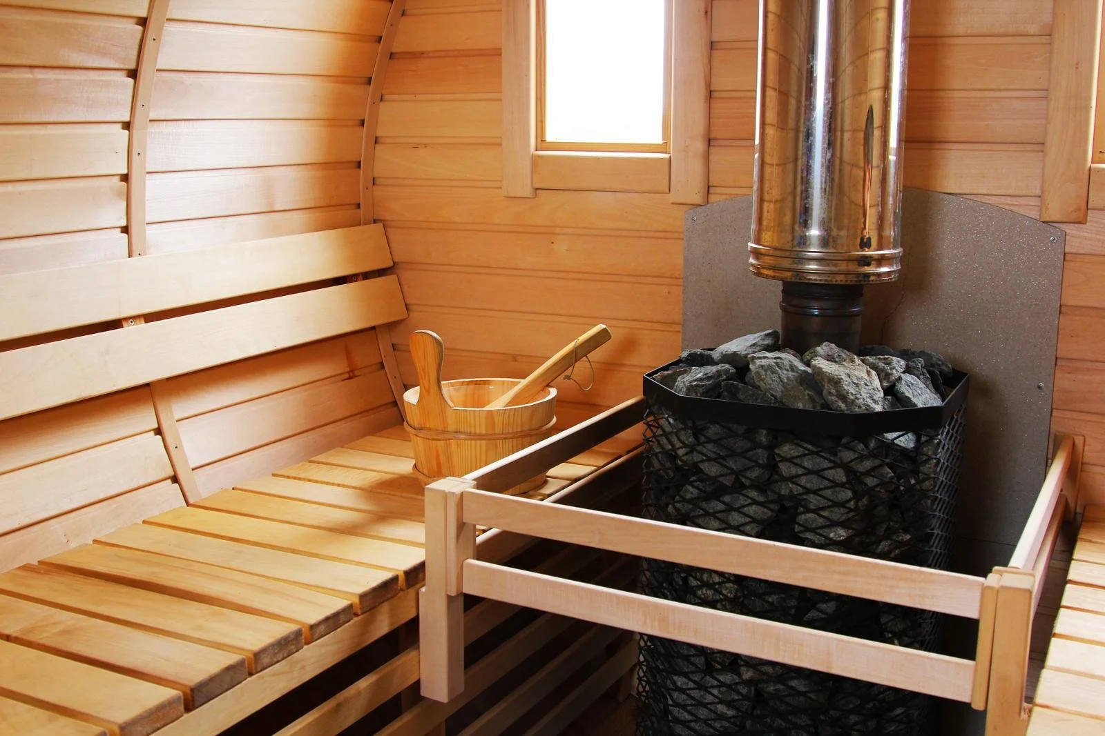 Wooden hot tub with a carved Om symbol on the side, covered with ice packs, set outdoors overlooking a grassy field, trees, and a sunrise or sunset sky.