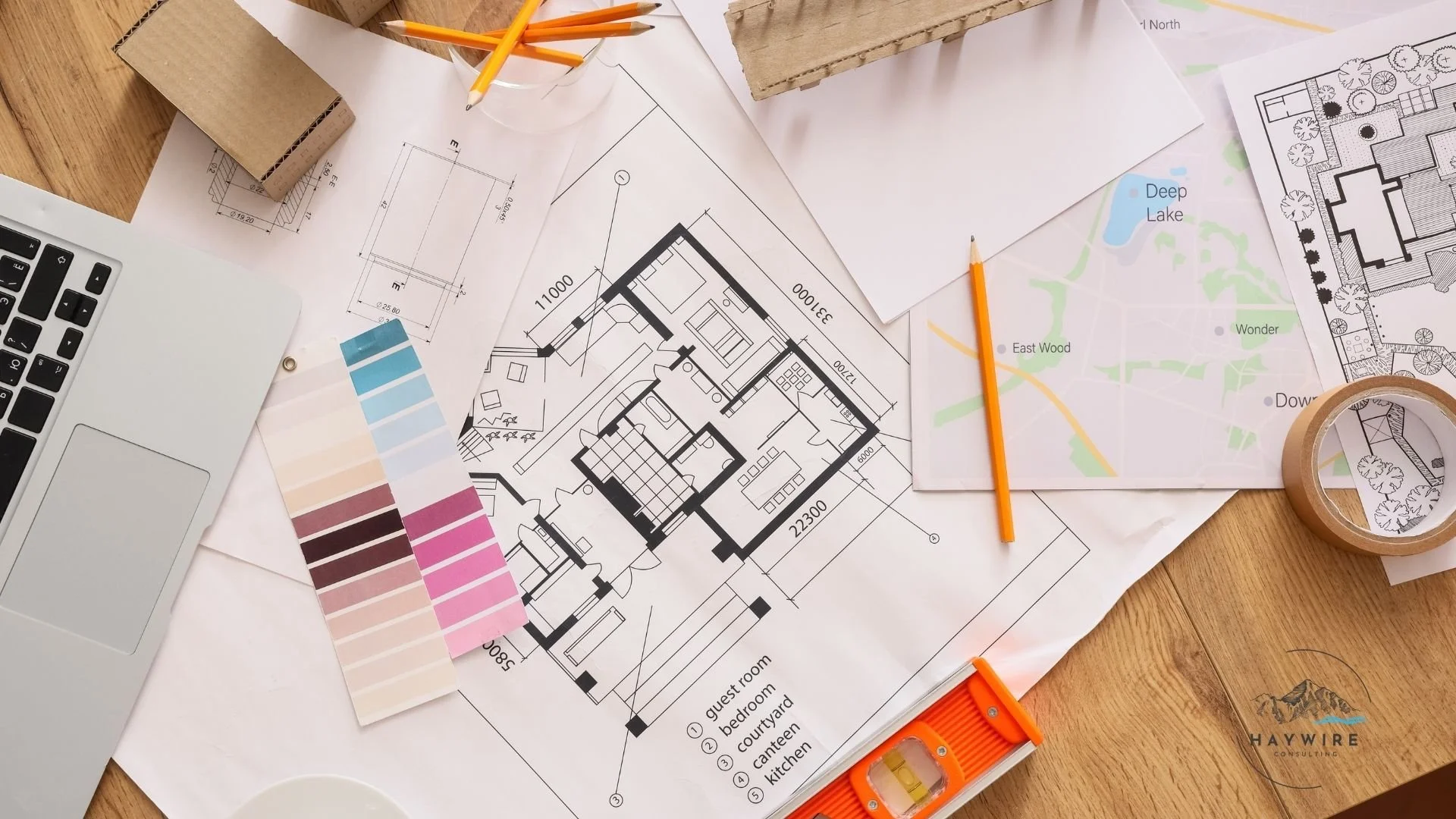 An overhead flat lay of an interior designer desk featuring architectural blueprints, a color swatch palette, pencils, and a laptop.