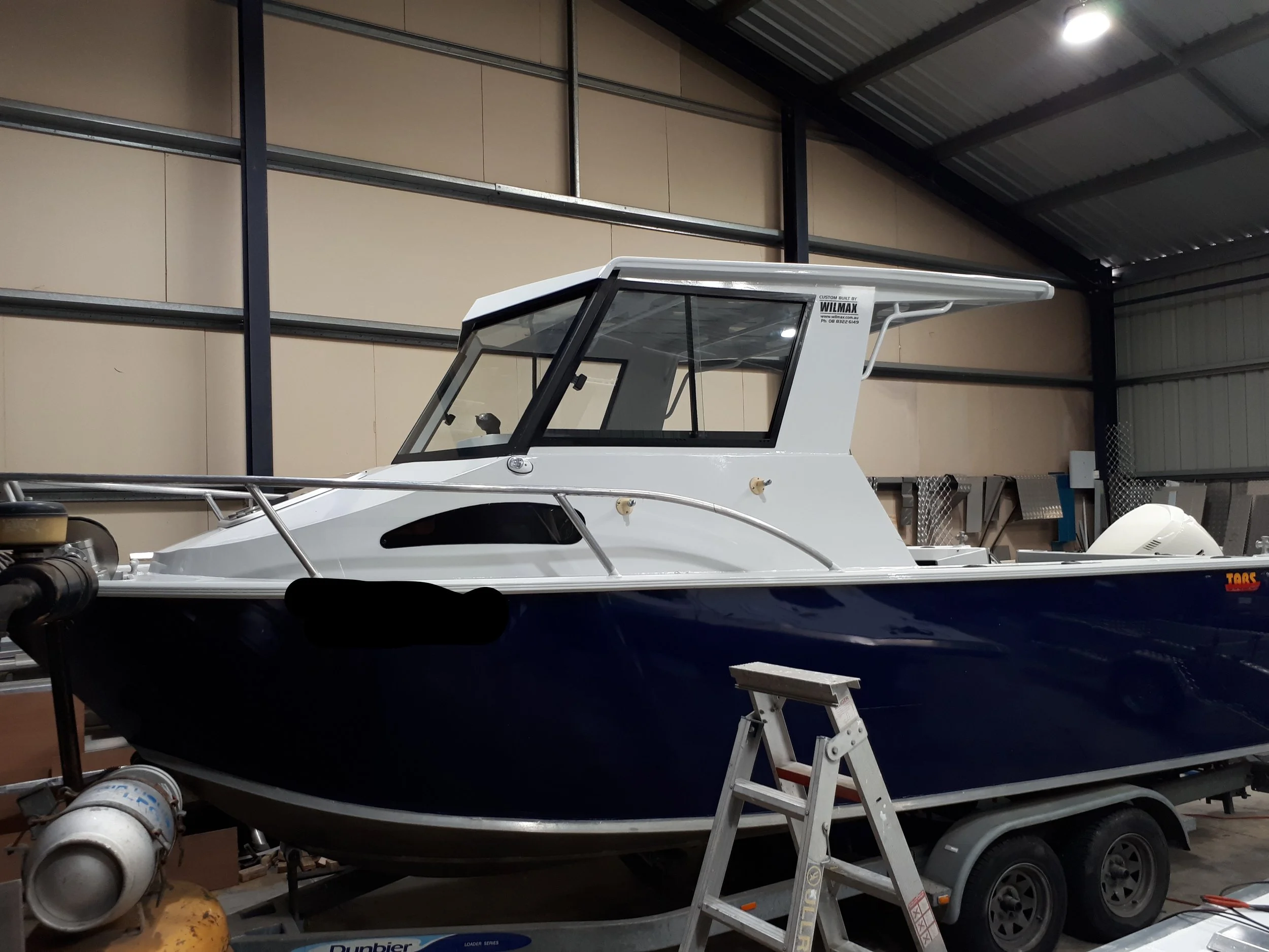 A white boat on a trailer inside a storage warehouse with a metal roof and beige walls.