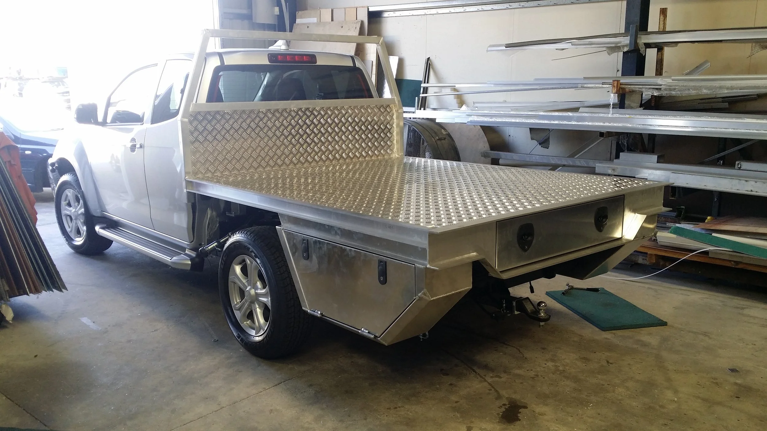 A silver pickup truck with a flatbed made of aluminum diamond plate parked inside a workshop or storage unit. with a custom canopy