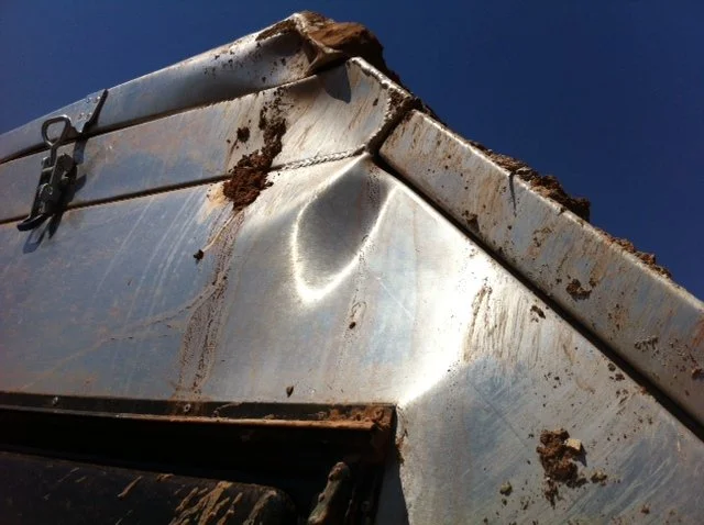 Close-up of a crashed caravan with dents and dirt against a blue sky.