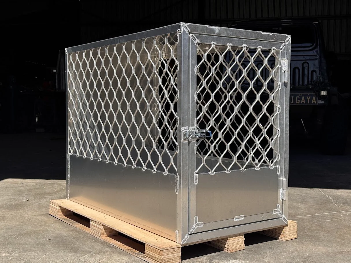 A silver metal cage with a lock, placed on a wooden pallet outside a building.