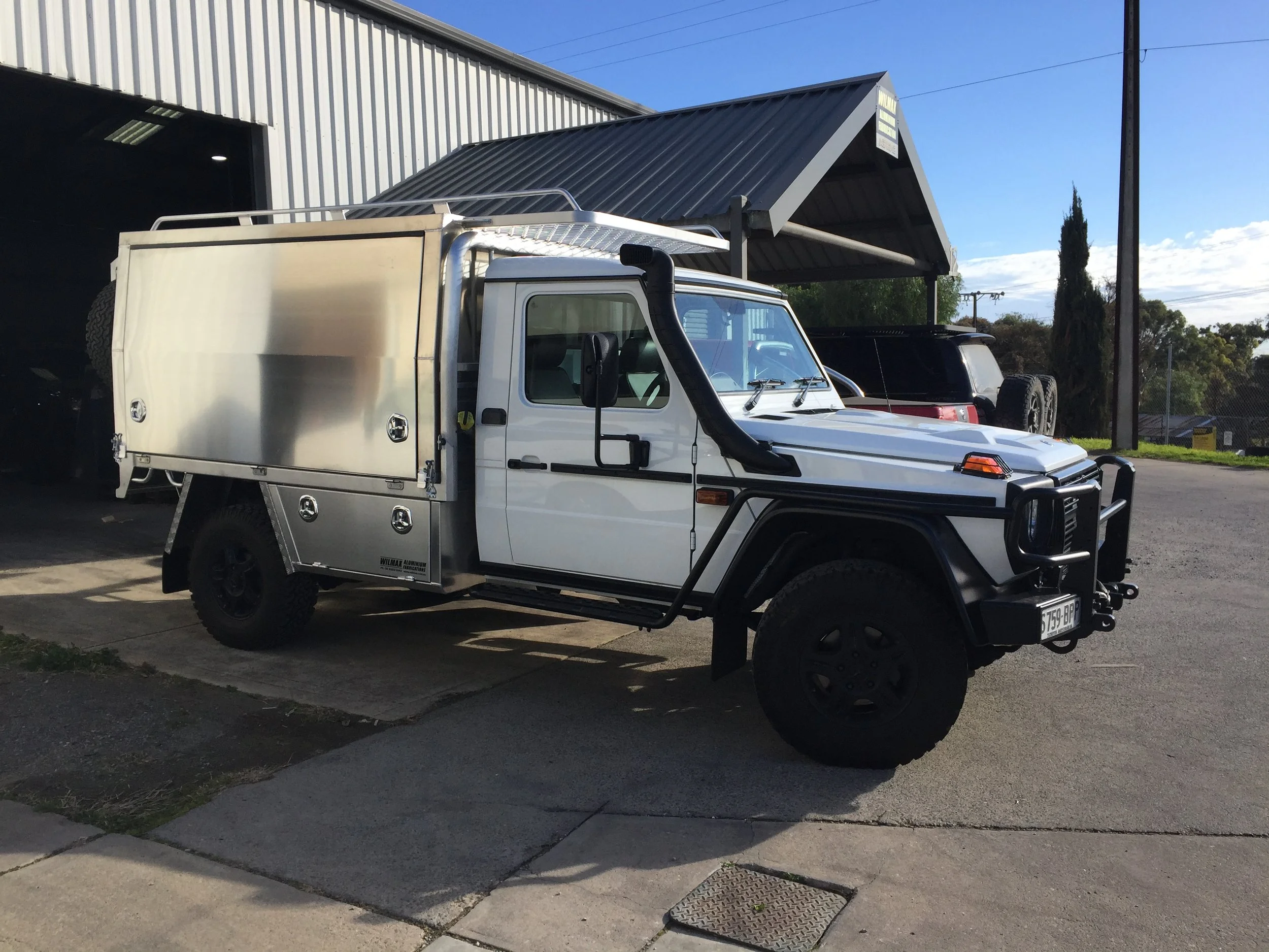 A white utility truck parked outdoors near a building with a dark gray roof, and a clear blue sky in the background.