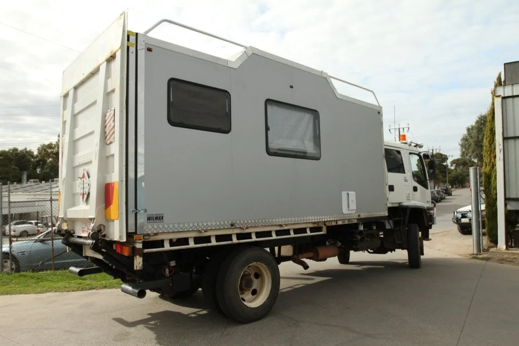 A white cargo truck with an attached gray camper parked on a street.