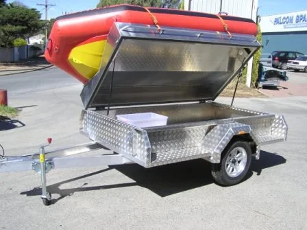 A custom aluminium utility trailer with a red boat mounted on top, parked on a street with buildings and cars in the background.