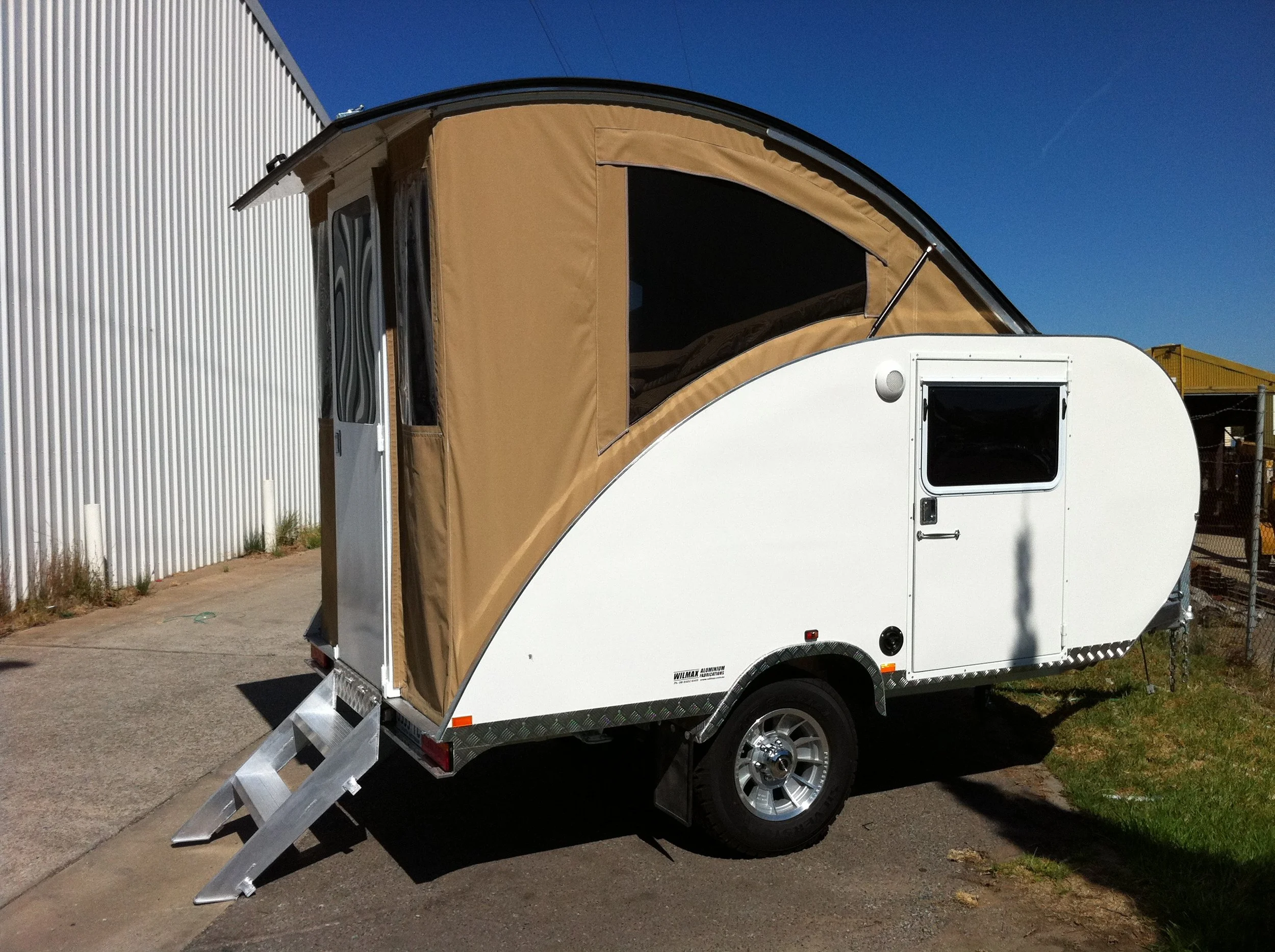 A small white travel trailer with a brown fabric tent extension on top, aerodynamic camper trailer.