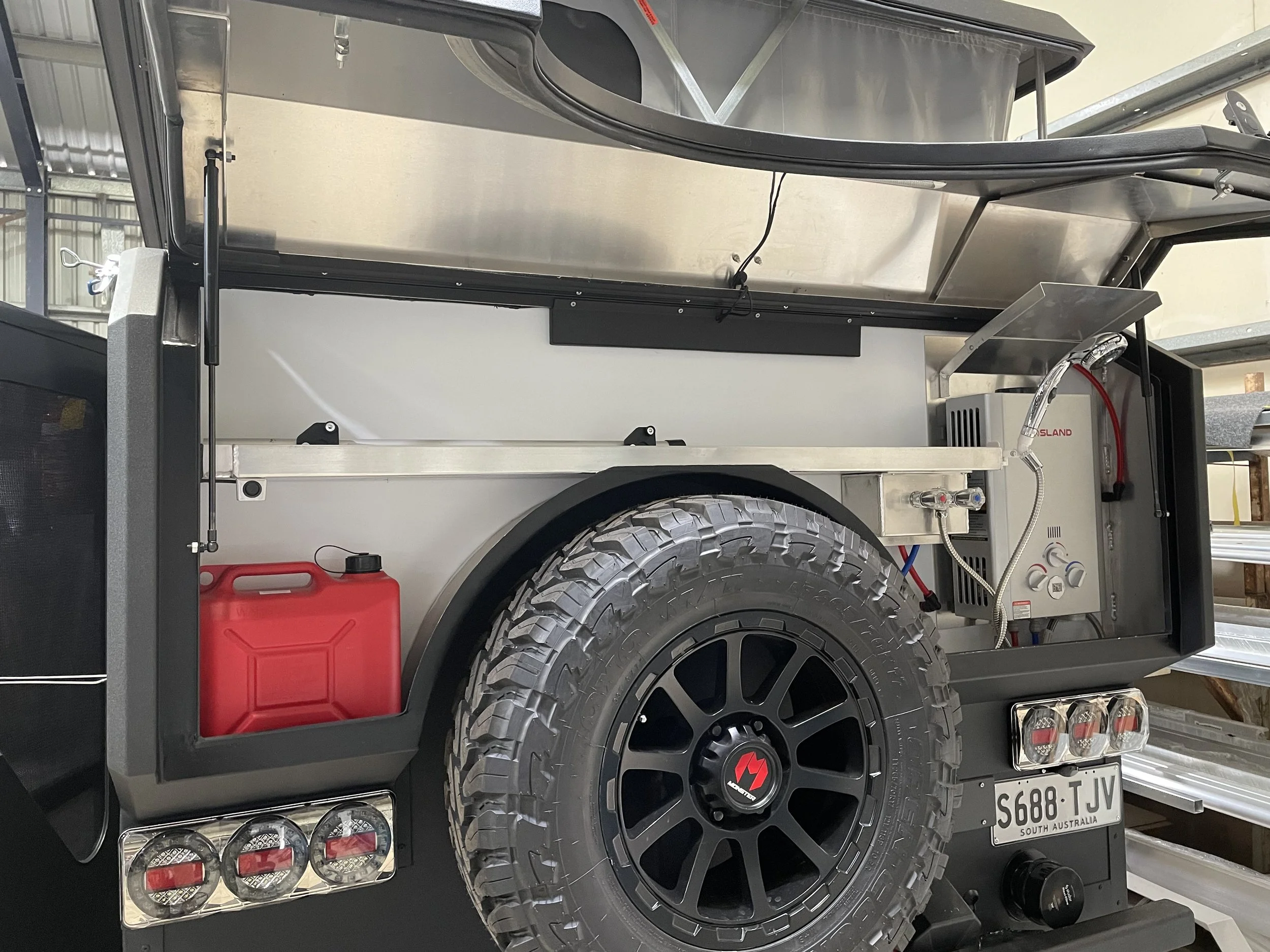 The rear of a custom caravan with a hot water system and storage for fuel. with a large spare wheel on the back