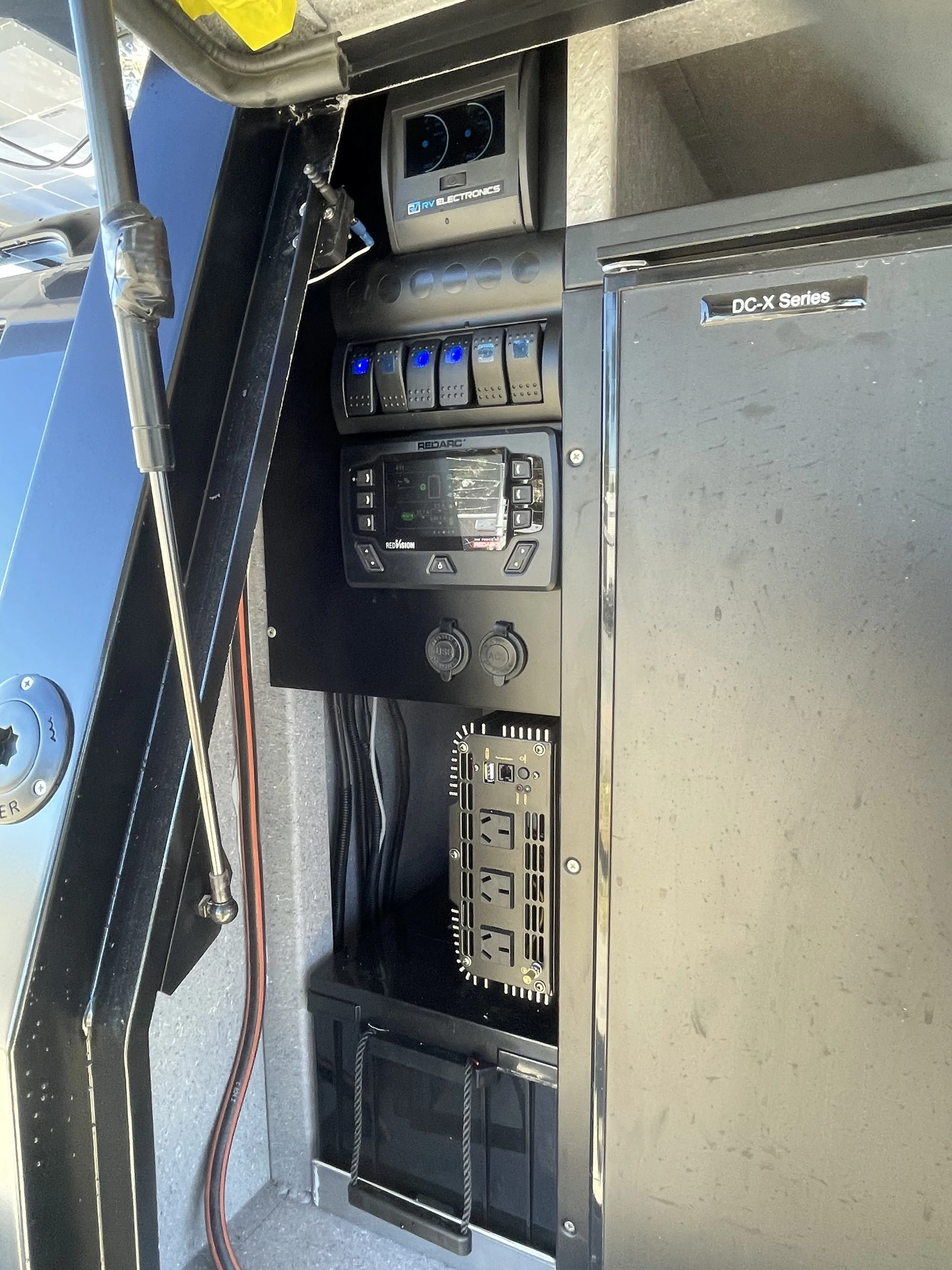 Inside view of a truck dashboard showing electronic and control components, with visible cables, power outlets, and a wire with a red and black cable.